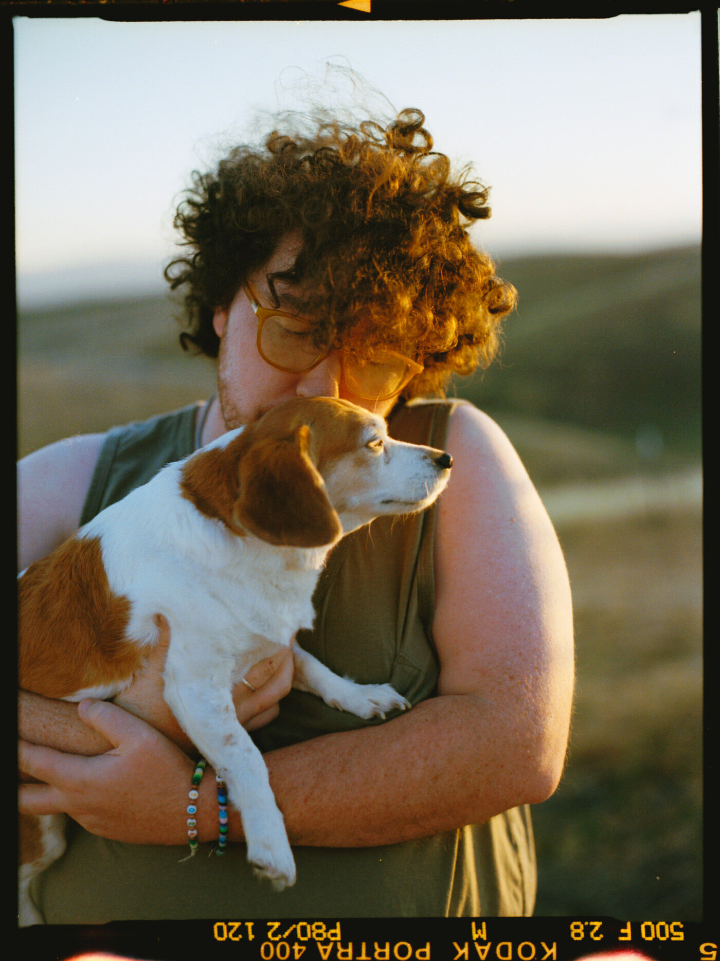 film photograph of man with curly hair hugging and holding dog at sunset