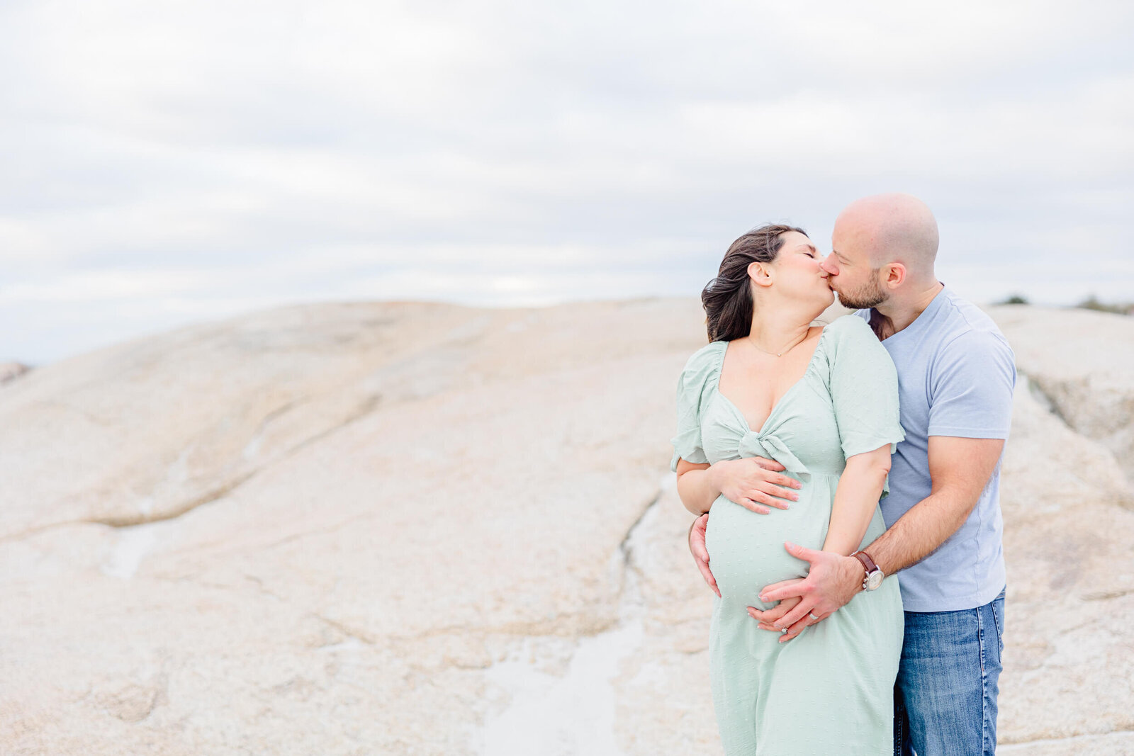 Pregnant woman and her husband, holding her baby bump from behind, share a kiss