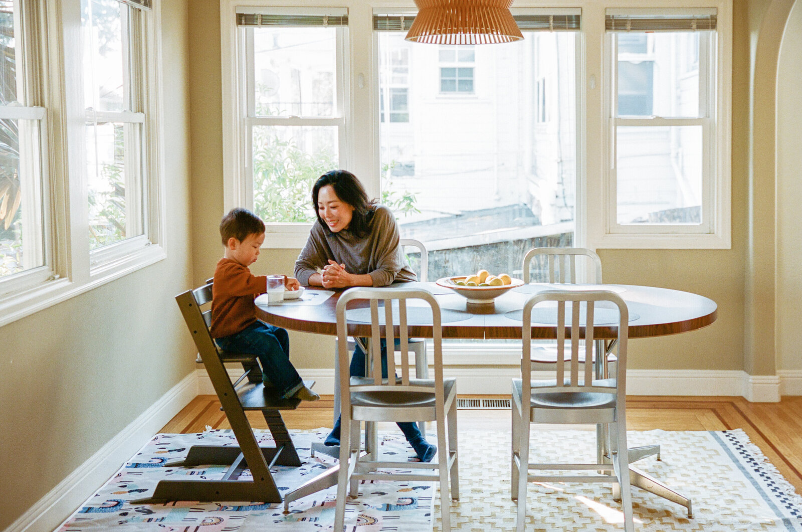Asian mom and toddler son sitting at dining table having a snack