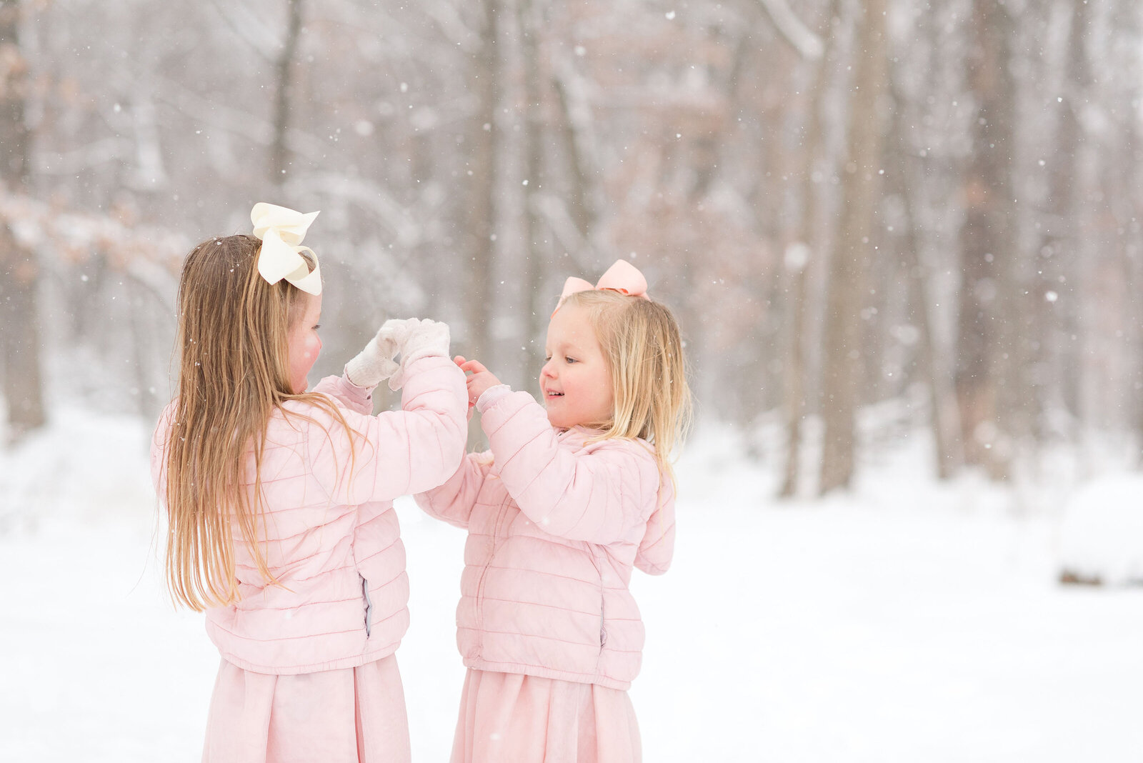 Two young sisters in pink coats play in snow