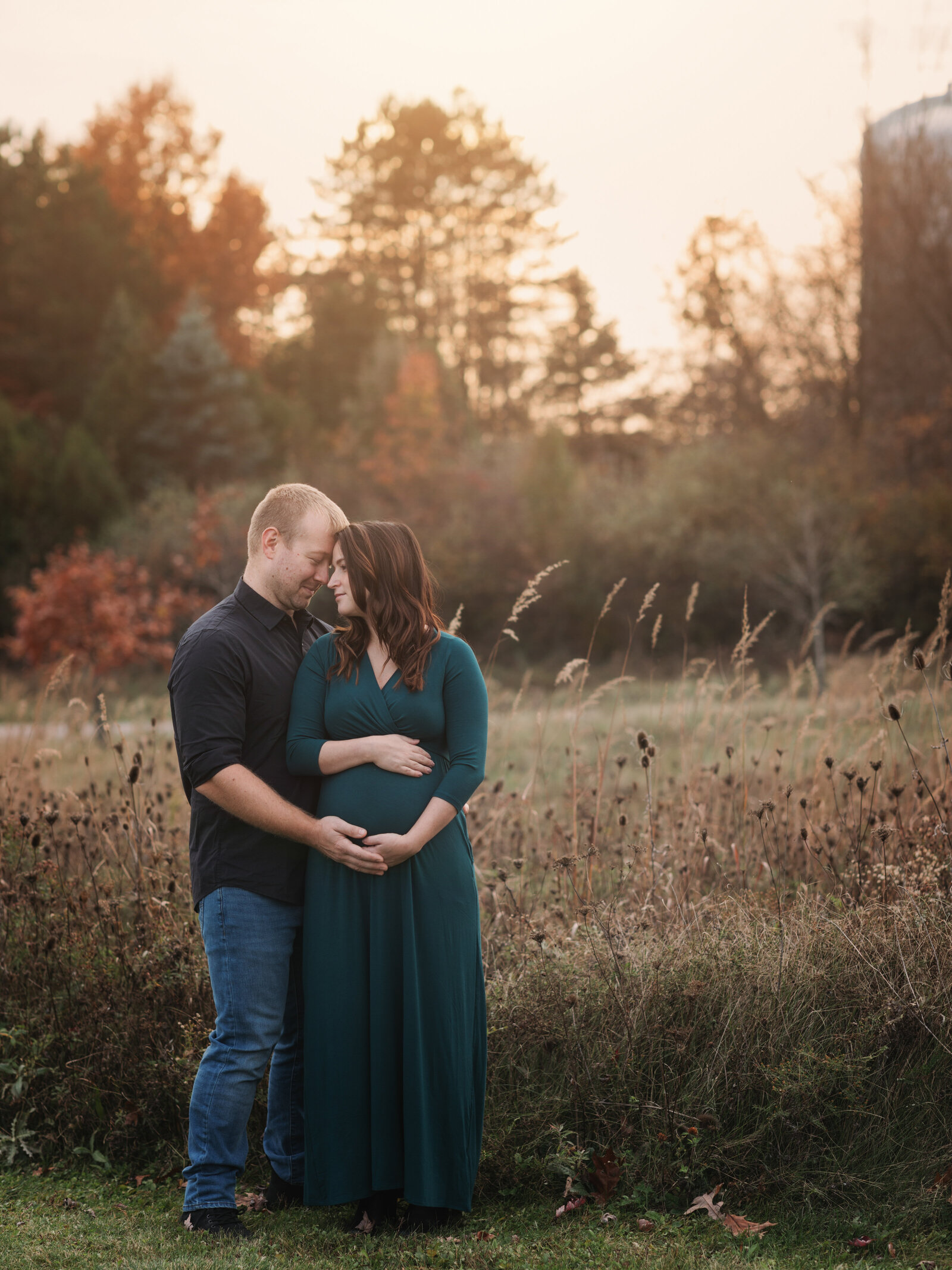 husband and pregant wife in green maternity gown holding baby bump for maternity portraits