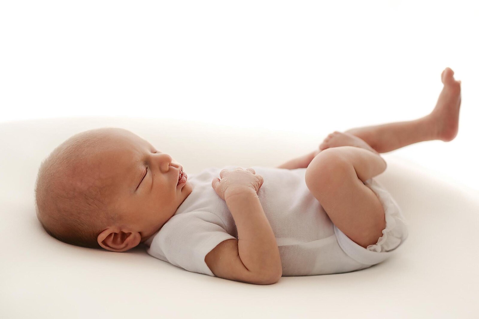a newborn sleeping in a simple white outfit