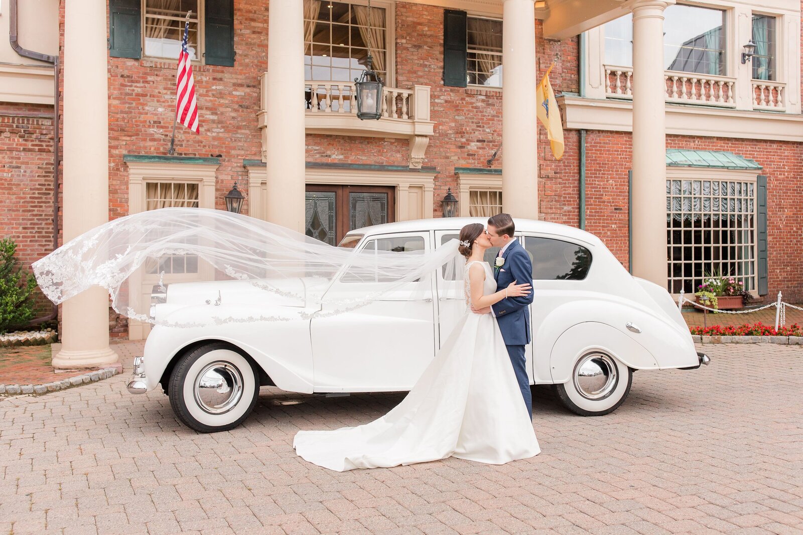 bride and groom kissing in front of a Rolls Royce with veil blowing in the wind