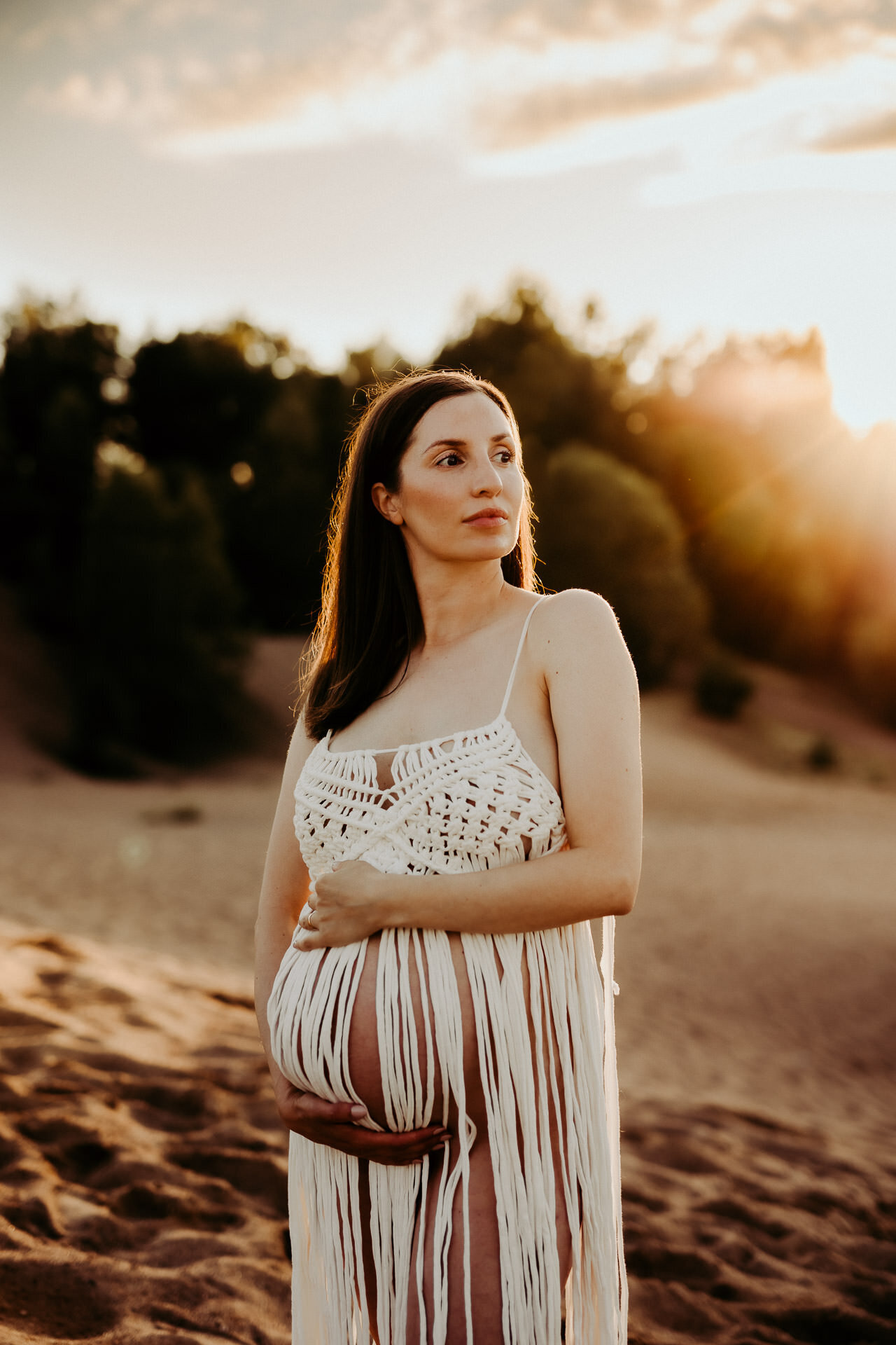 en gravid mamma håller om sin mage bland sanddyner i solnedgången