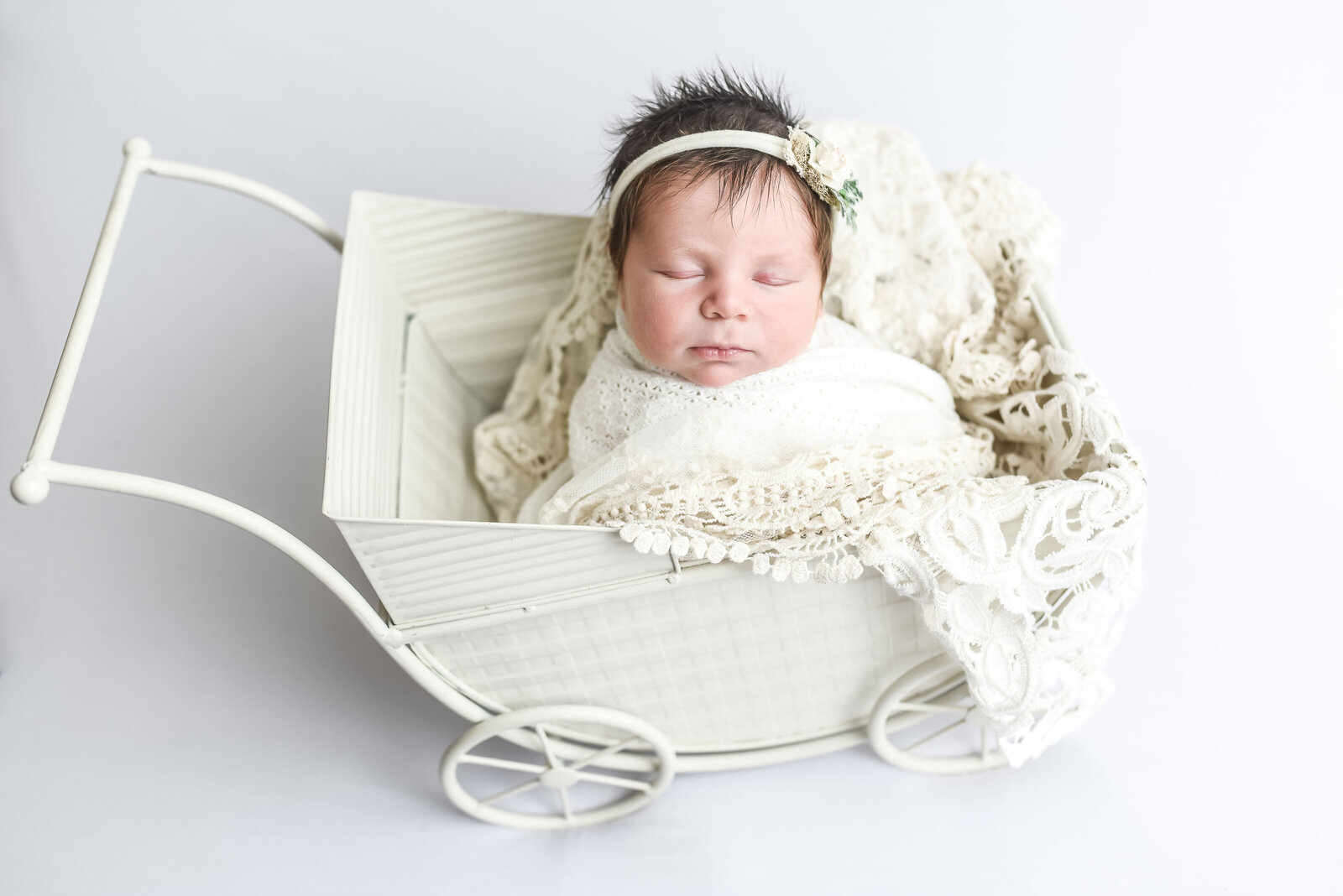 newborn baby laying in white buggy  with white blanket