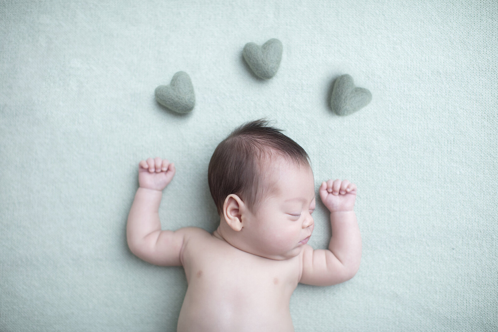 Newborn boy on green fabric with hearts.