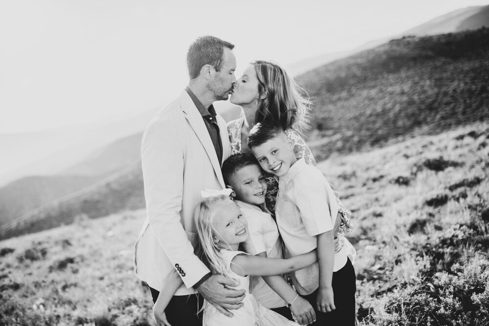 Mom and Dad go in for a kiss while three children smile at them