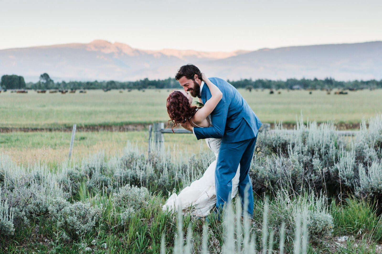 A groom dips his bride in a sagebrush field outside of Grand Teton National Park