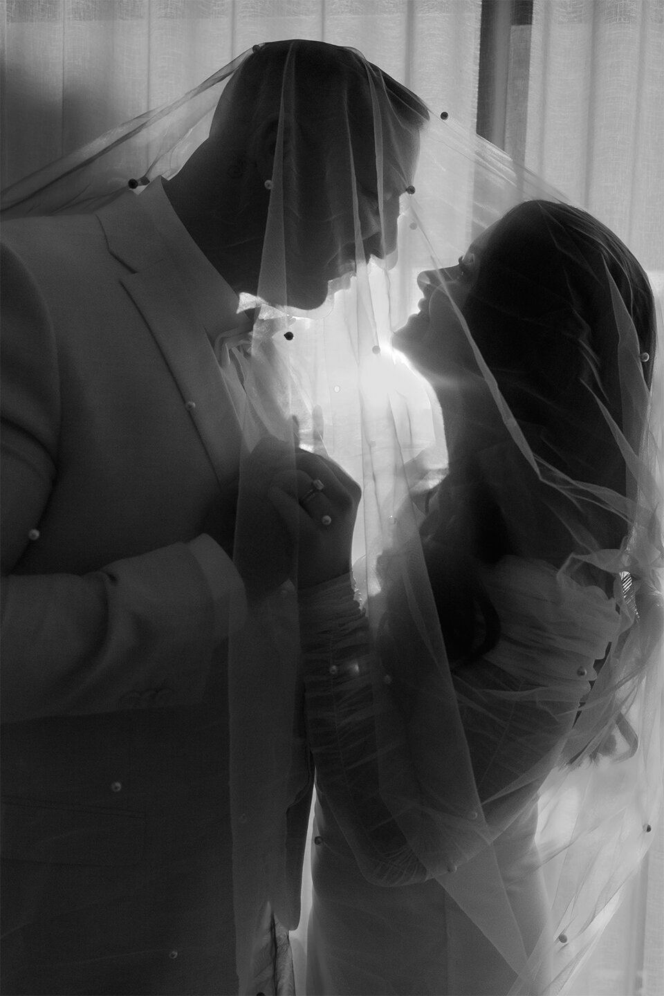 During their elopement, a bride and groom pose for a photo under the bride's pearl wedding veil. Taken in Perth, Western Australia.