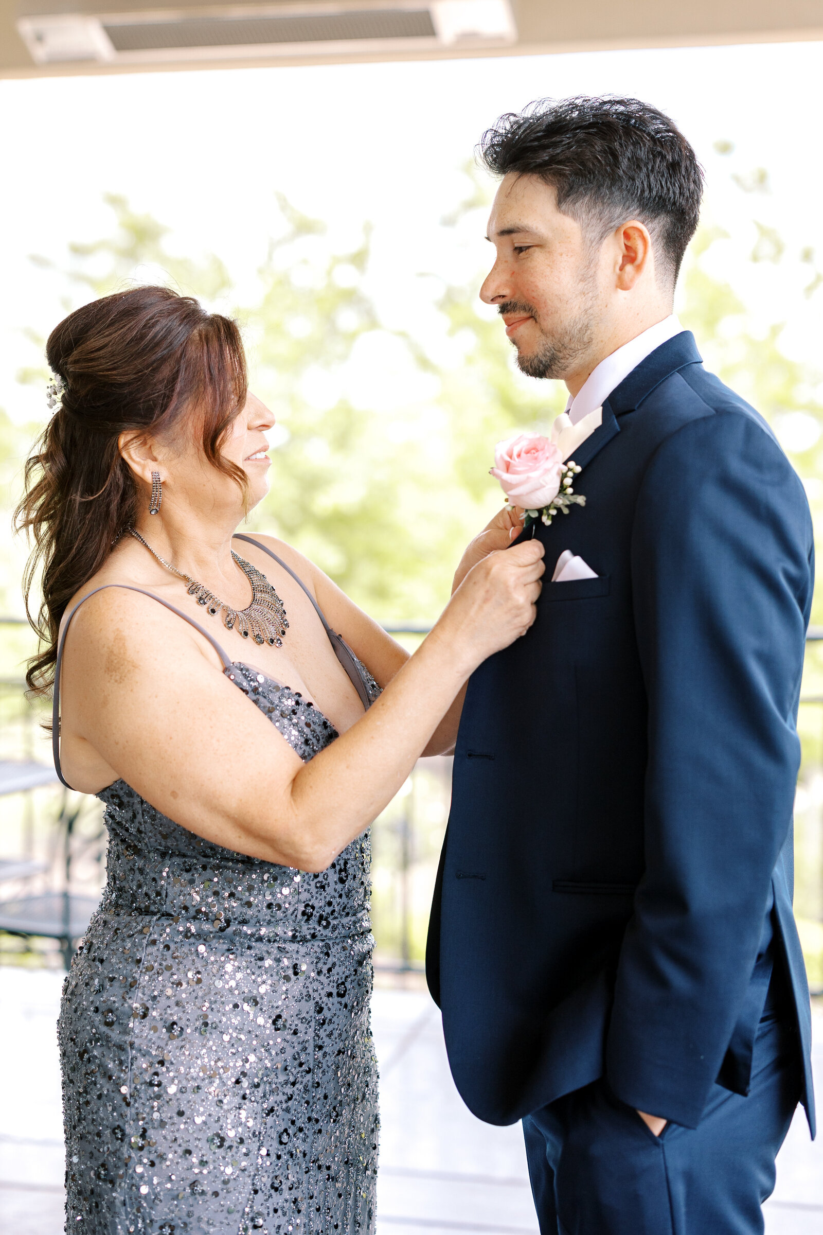 candid wedding photo of groom's mother putting on the groom's boutonniere while on a patio together captured by sacramento wedding photographer