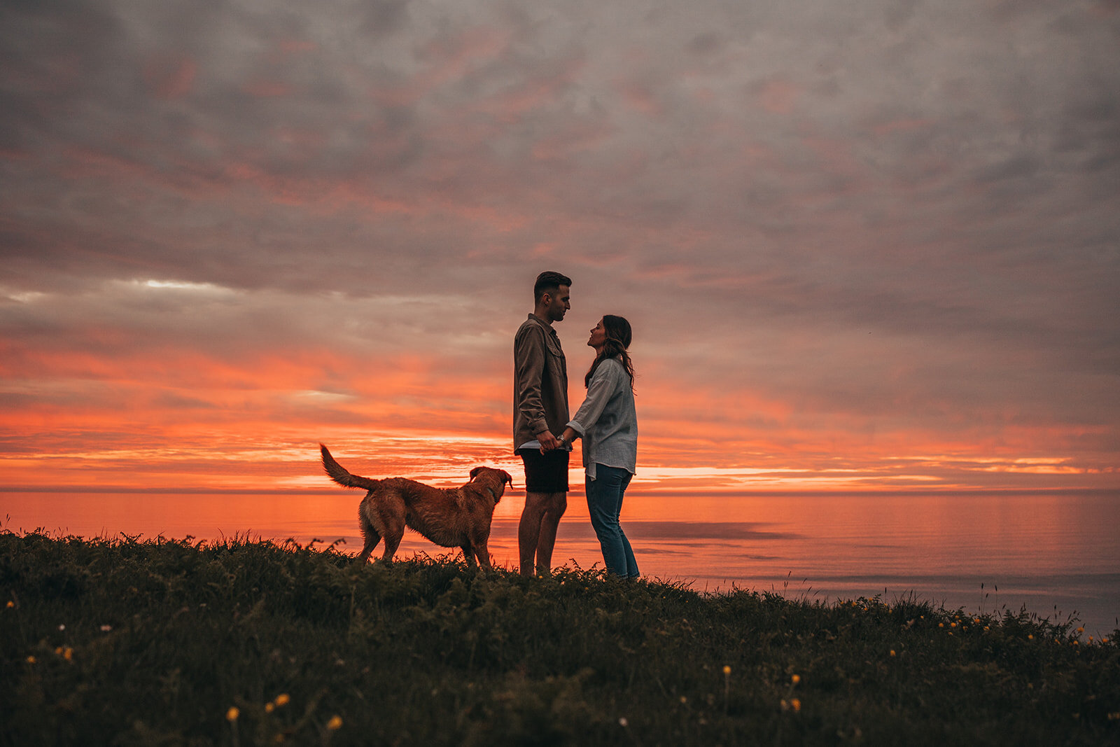 couple pose with dog at sunset