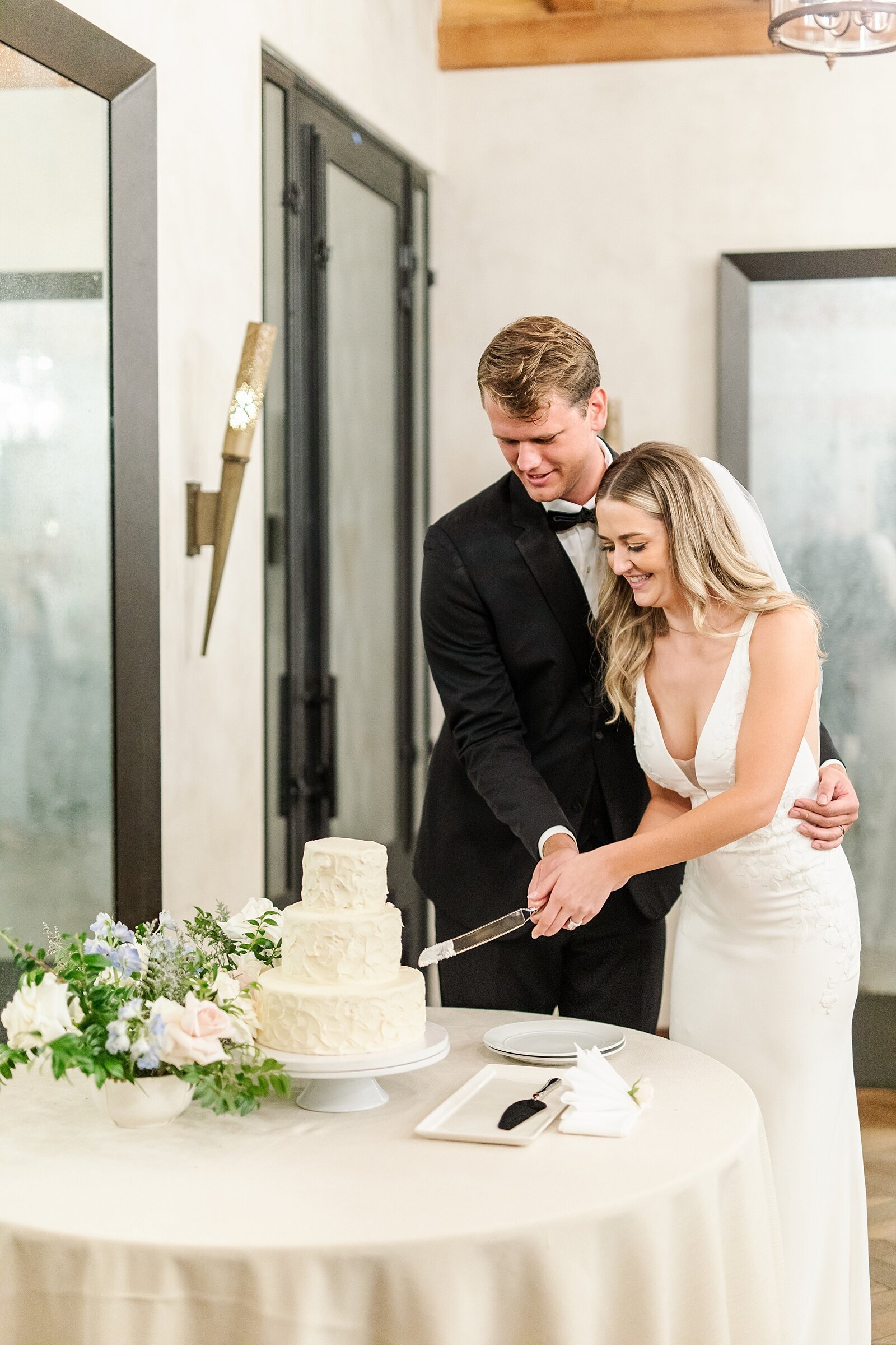 Bride and groom cutting white textured wedding cake inside Rancho Valencia in Rancho Sante Fe.