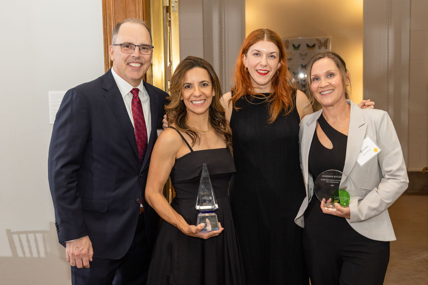 Group of four smiling people holding awards at a formal event
