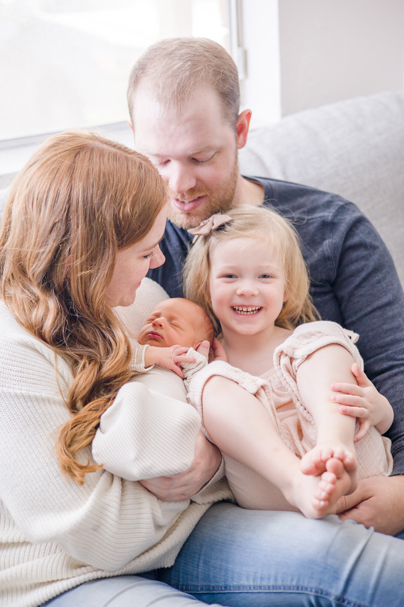 happy family on the couch laughing and smiling during their lifestyle in home newborn session with las vegas newborn photographer Jessica Bowles