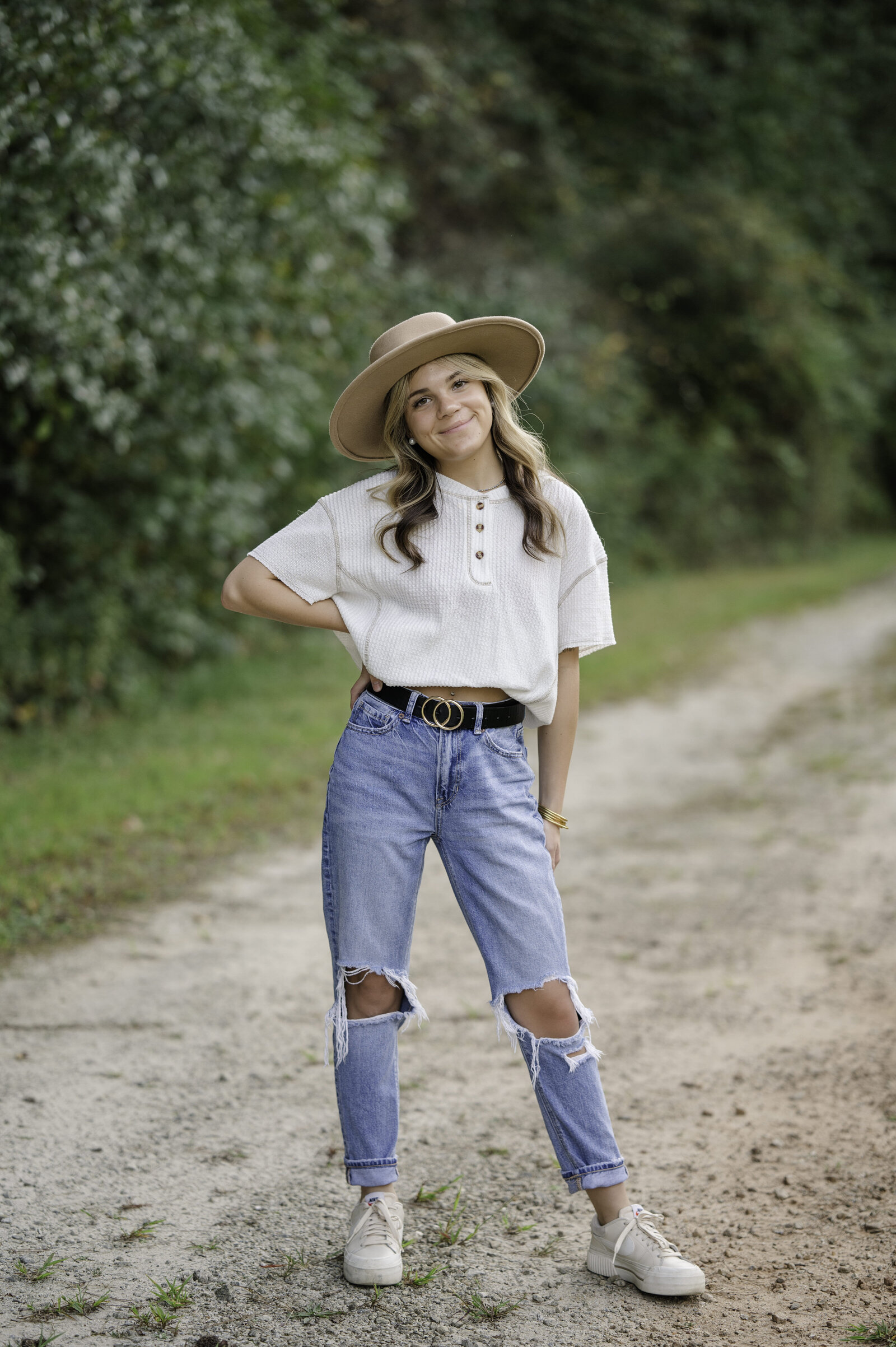 Social Circle High senior smiles while standing on the gravel path wearing a brown hat and ripped jeans