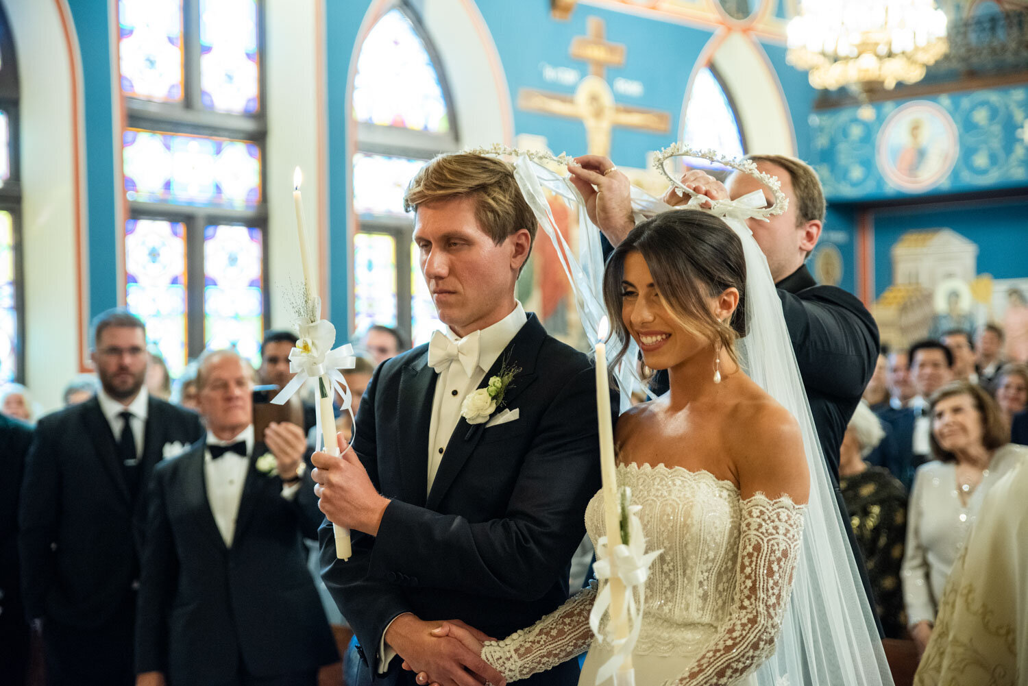 A bride and groom are standing in a church holding candles