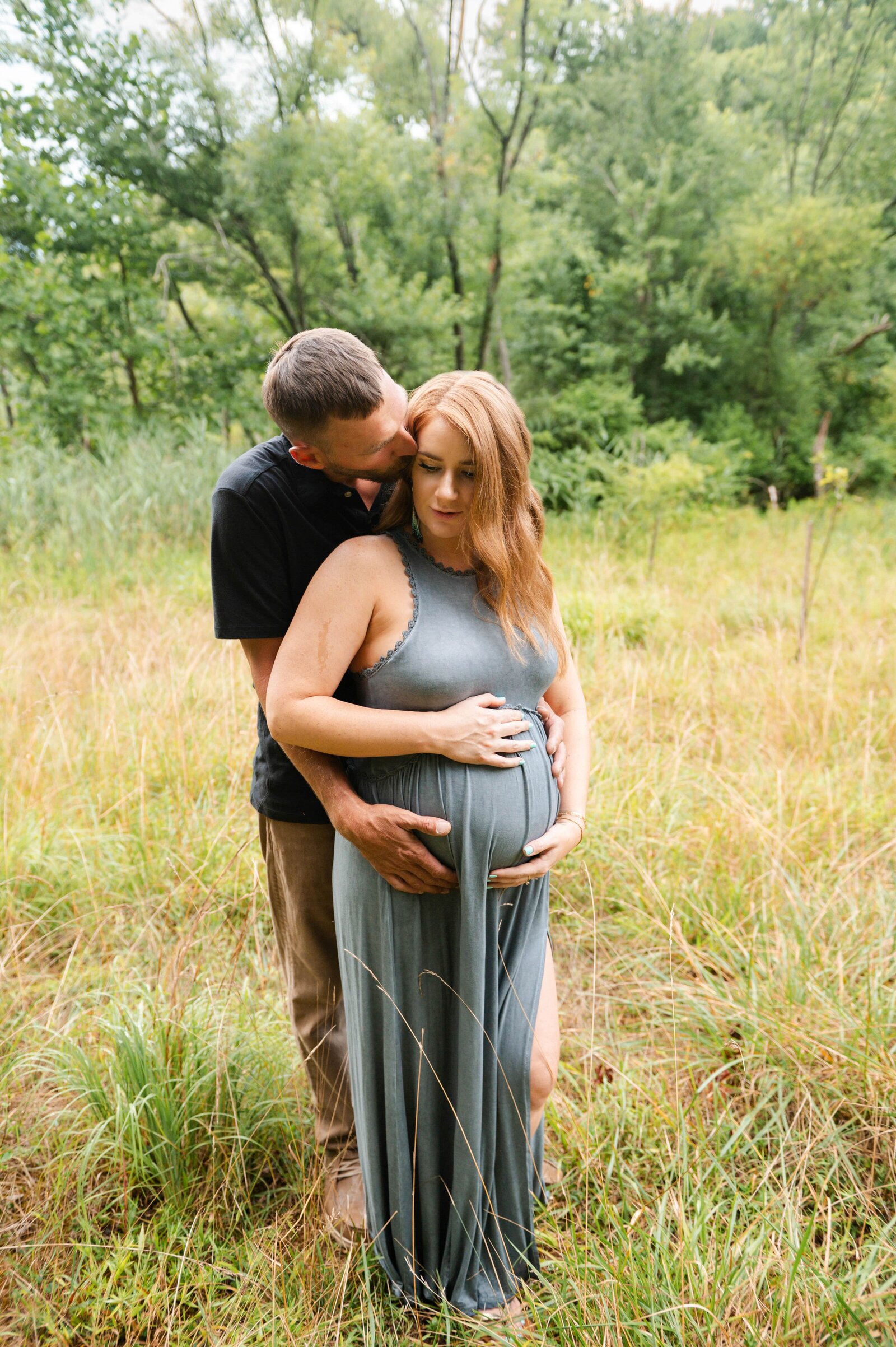 woman and man cuddling in grass during a pregnancy photoshoot