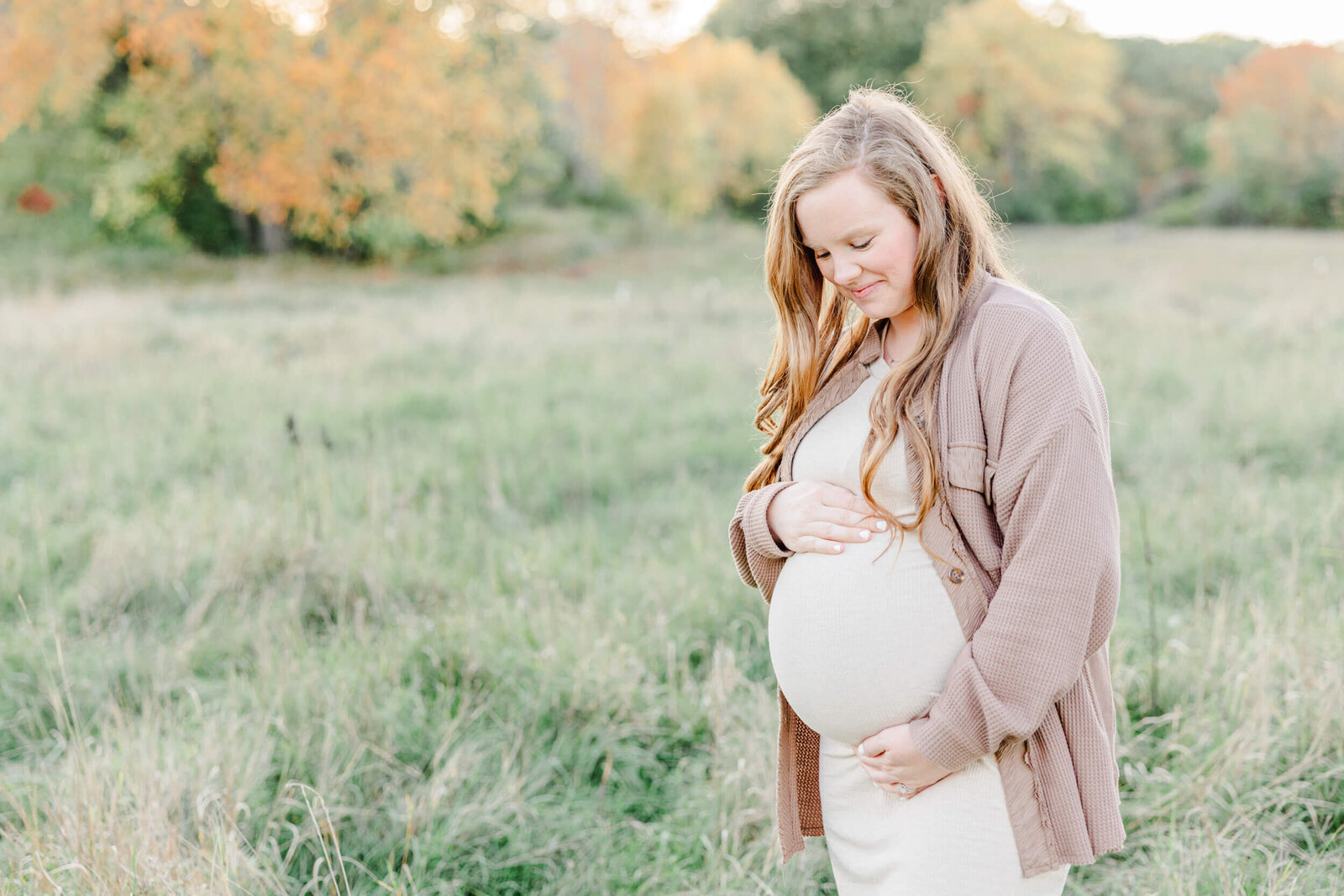 Pregnant woman in a meadow cradles her bump and smiles