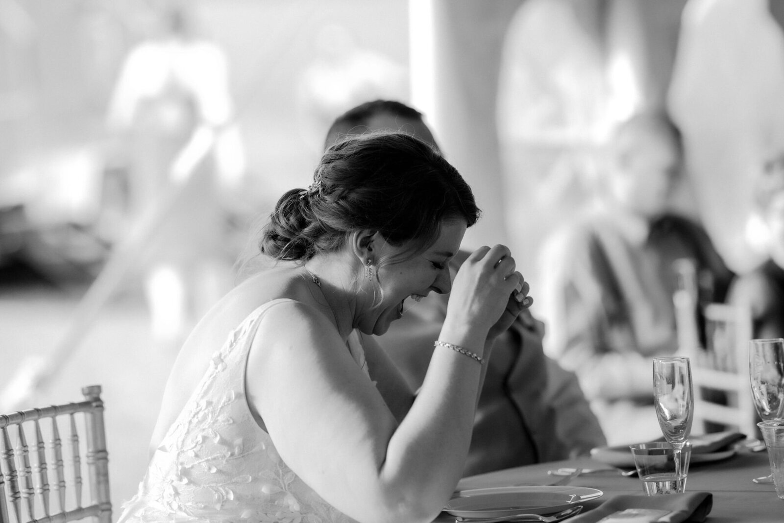 bride laughing covering face with hands while sitting at table during wedding reception