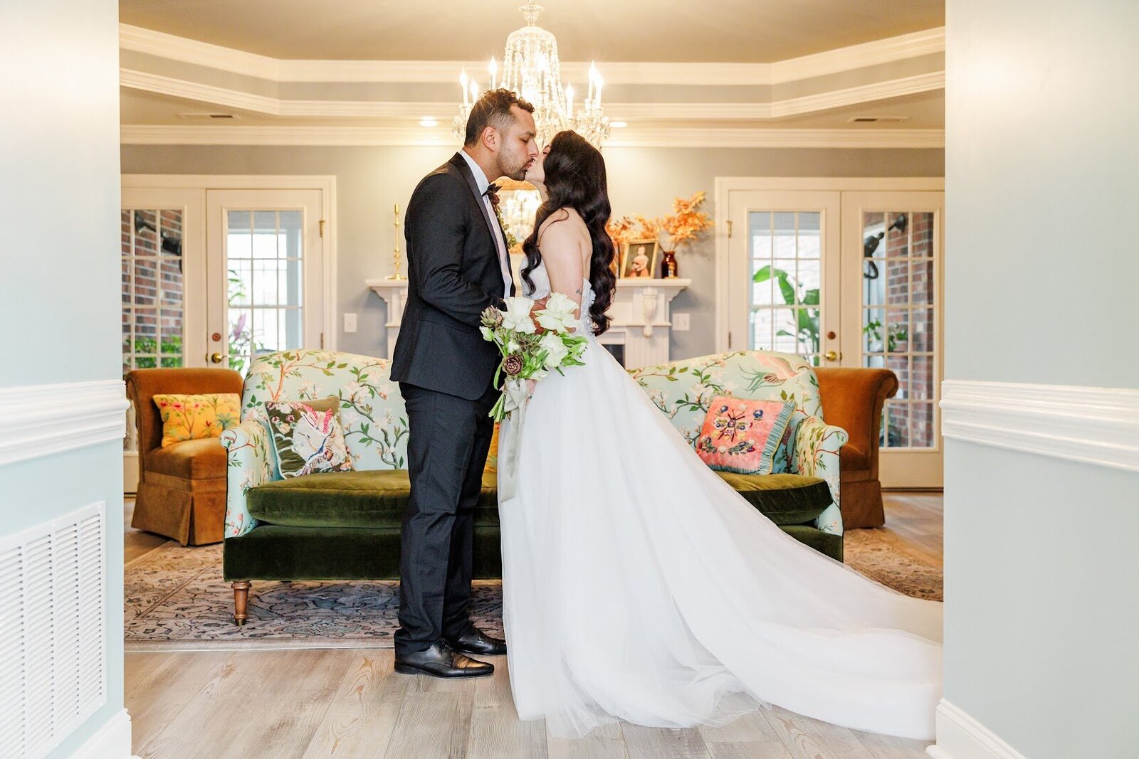 Bride and groom sharing a romantic moment under the chandelier, in the living room at The Retreat at Willow and Stone Events, with views into the sunroom.