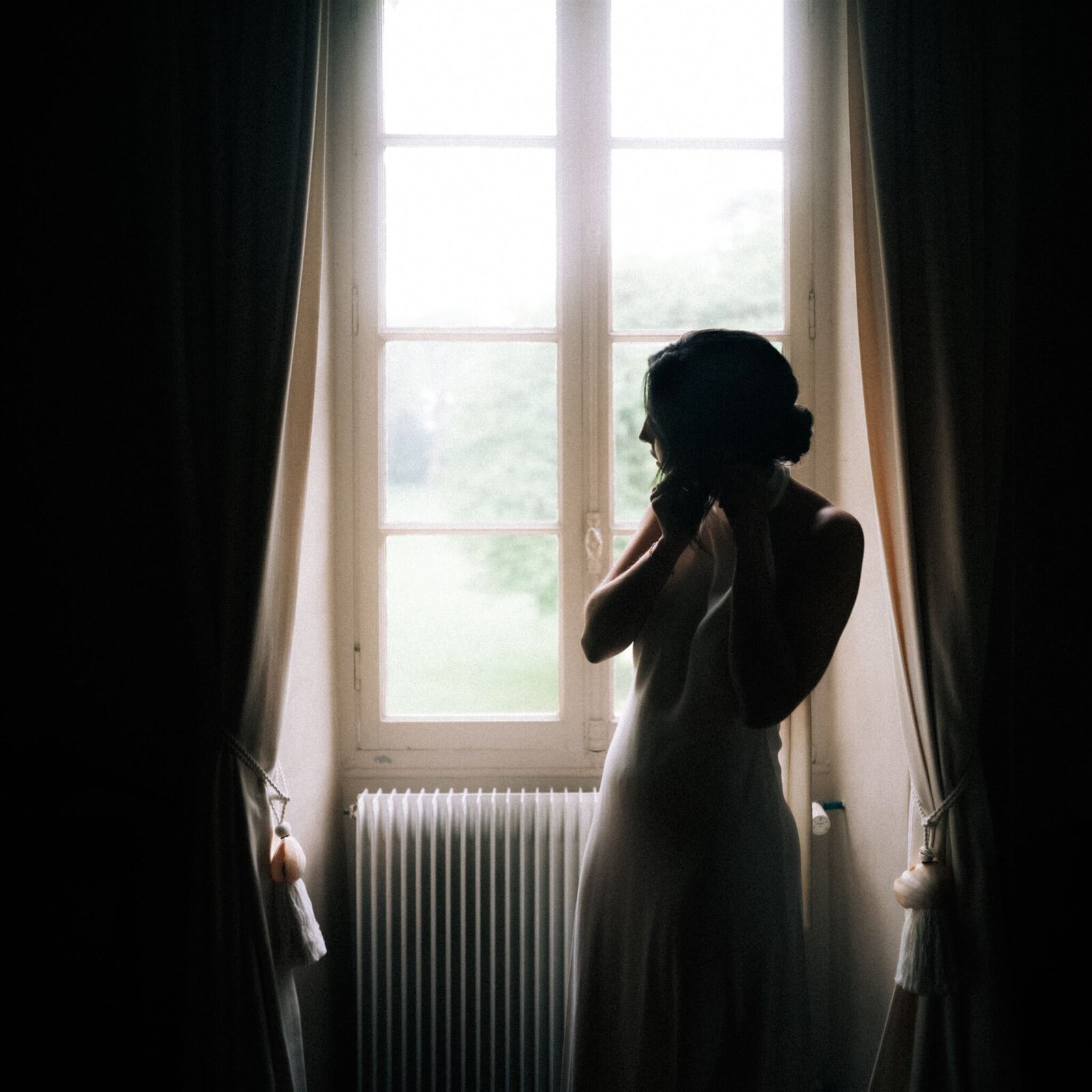 Bride putting earings by the window, surrounded by beautiful natural light