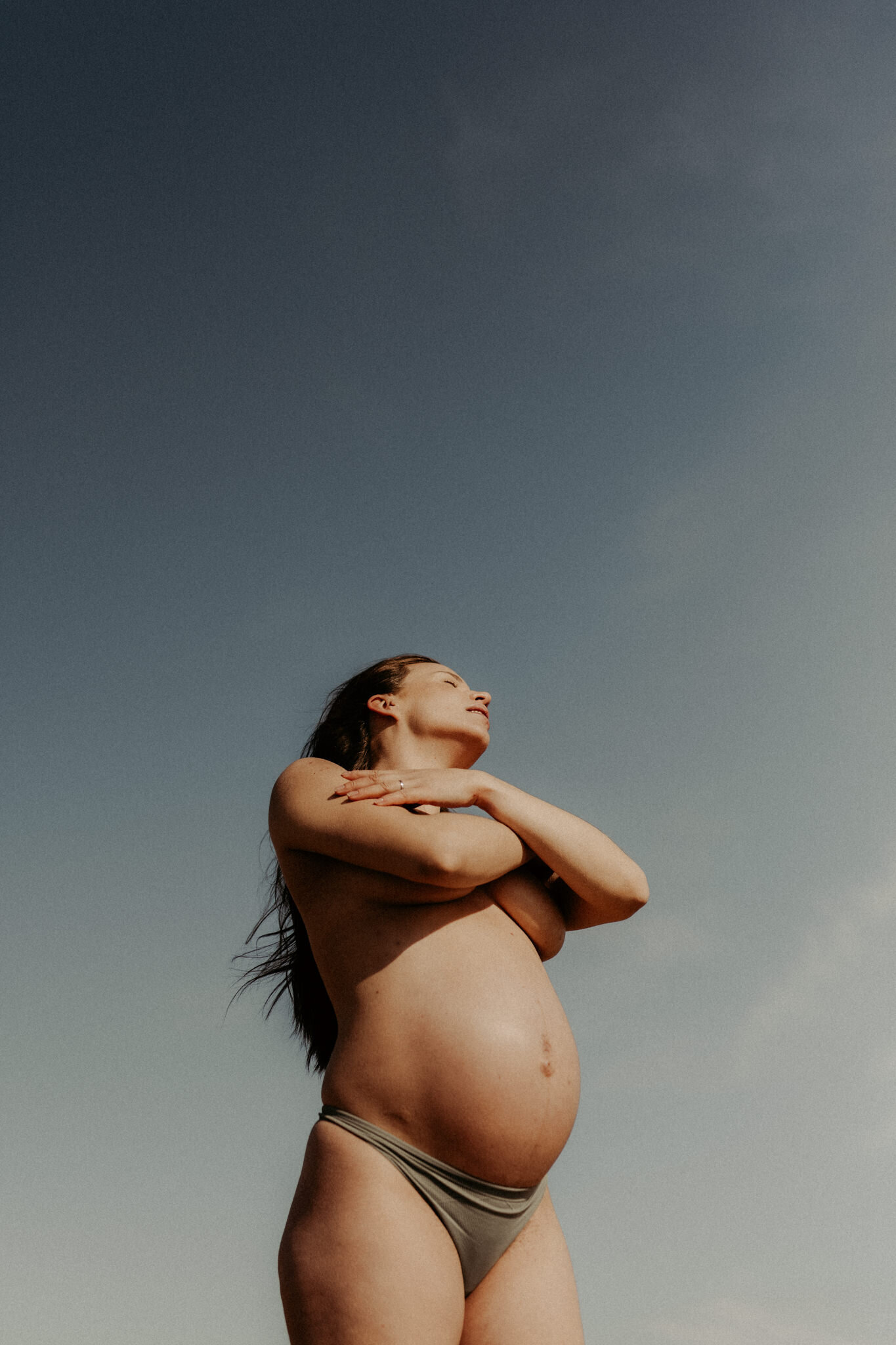 en gravid mamma står i bikini och blundar i solen