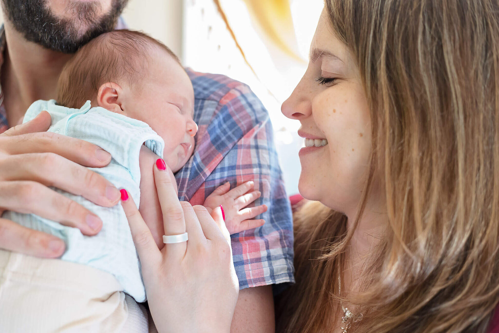 A close-up of a mom smiling at her newborn while dad holds the baby on his shoulder.