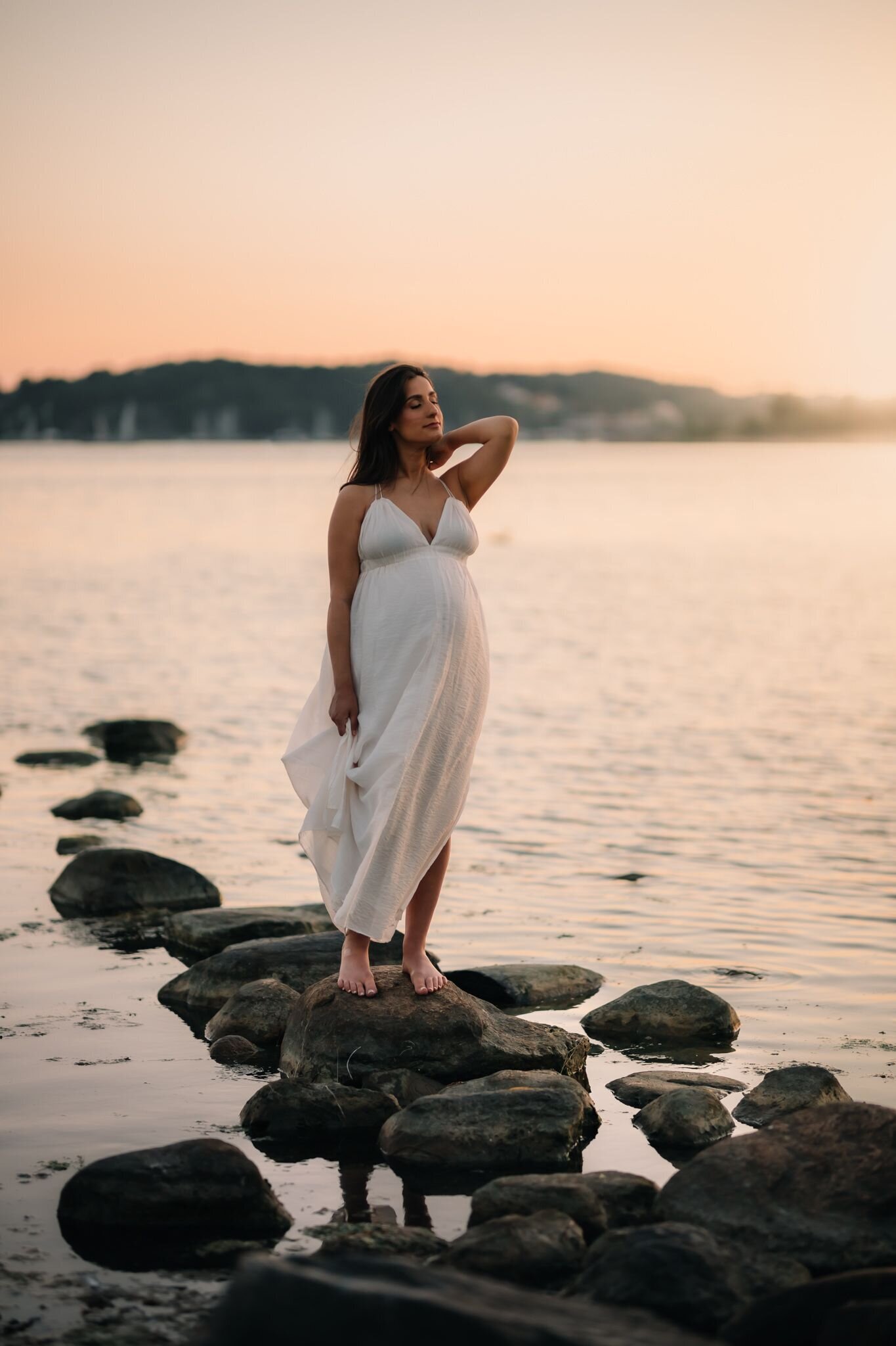 en gravid mamma står på stenar ute i vattnet och blundar mor solen