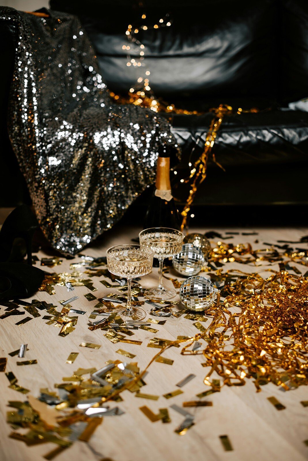 Champagne glasses, disco balls, and gold confetti on a party floor