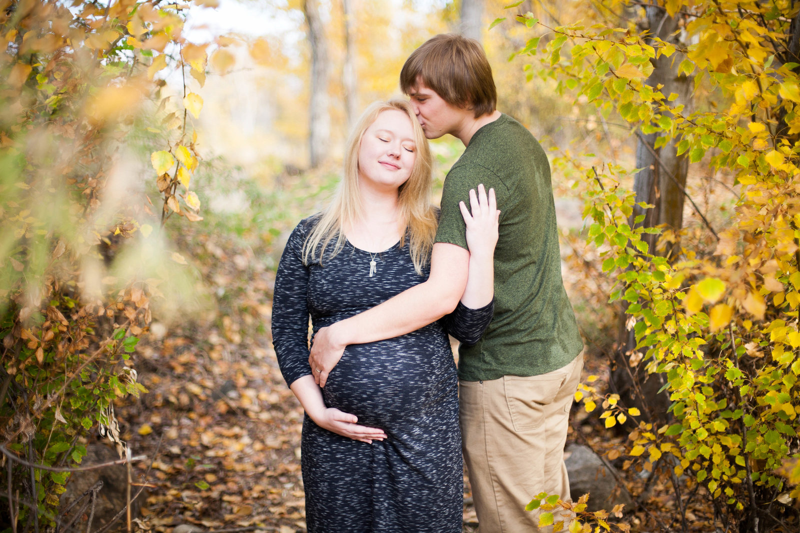 A man kissing his pregnant wife on her head.