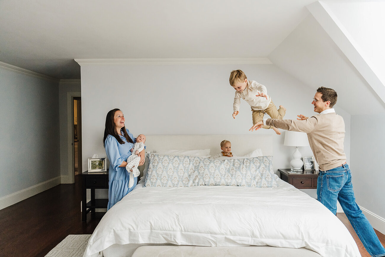 mom holds new baby brother while dad throws big brother onto bed