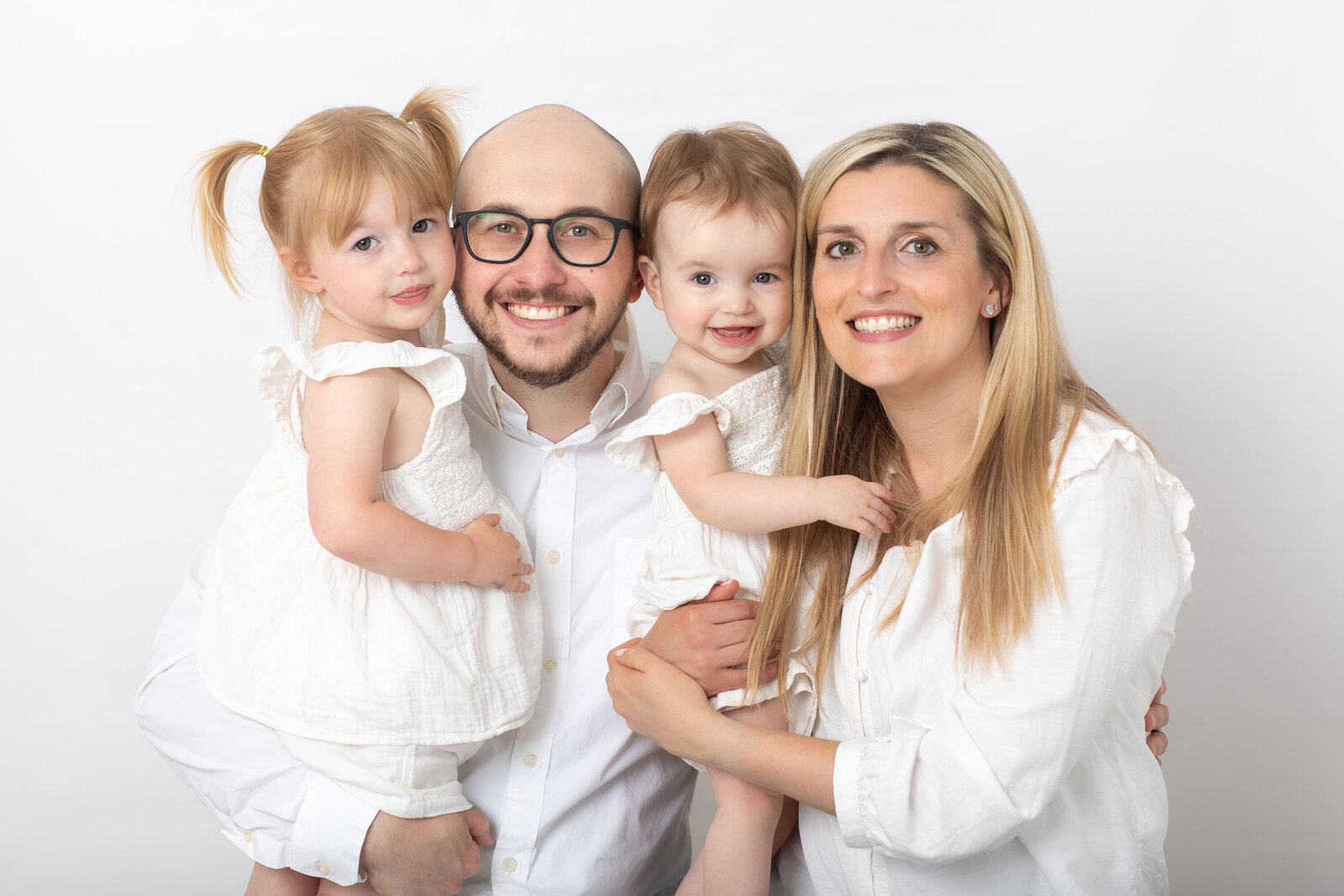 Family of four with mom, dad, and two toddlers sitting closely together, sharing a joyful moment