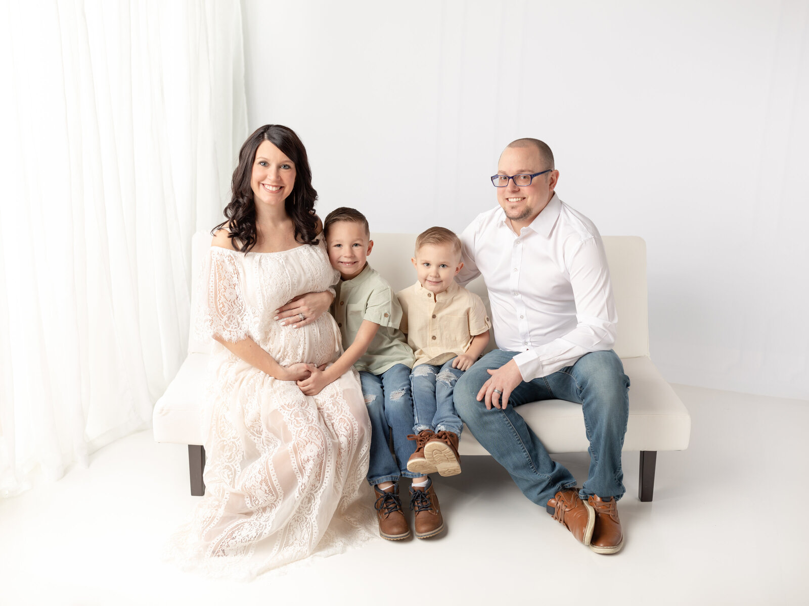 pregnant mother and family sitting on white futon for photoshoot cleveland maternity photographer