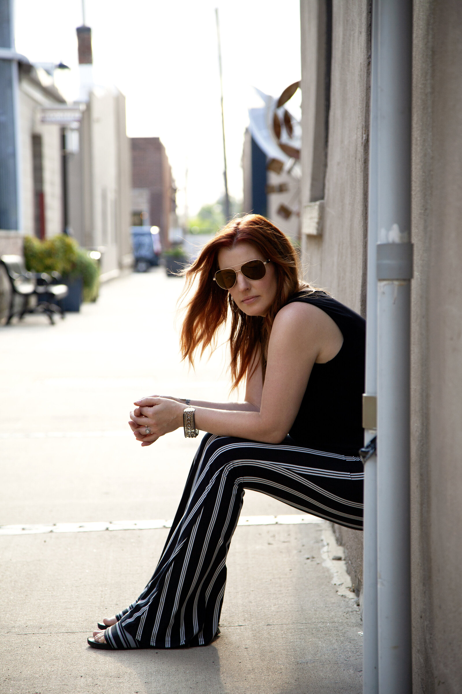 Woman with red hair and aviators sitting in alleyway.