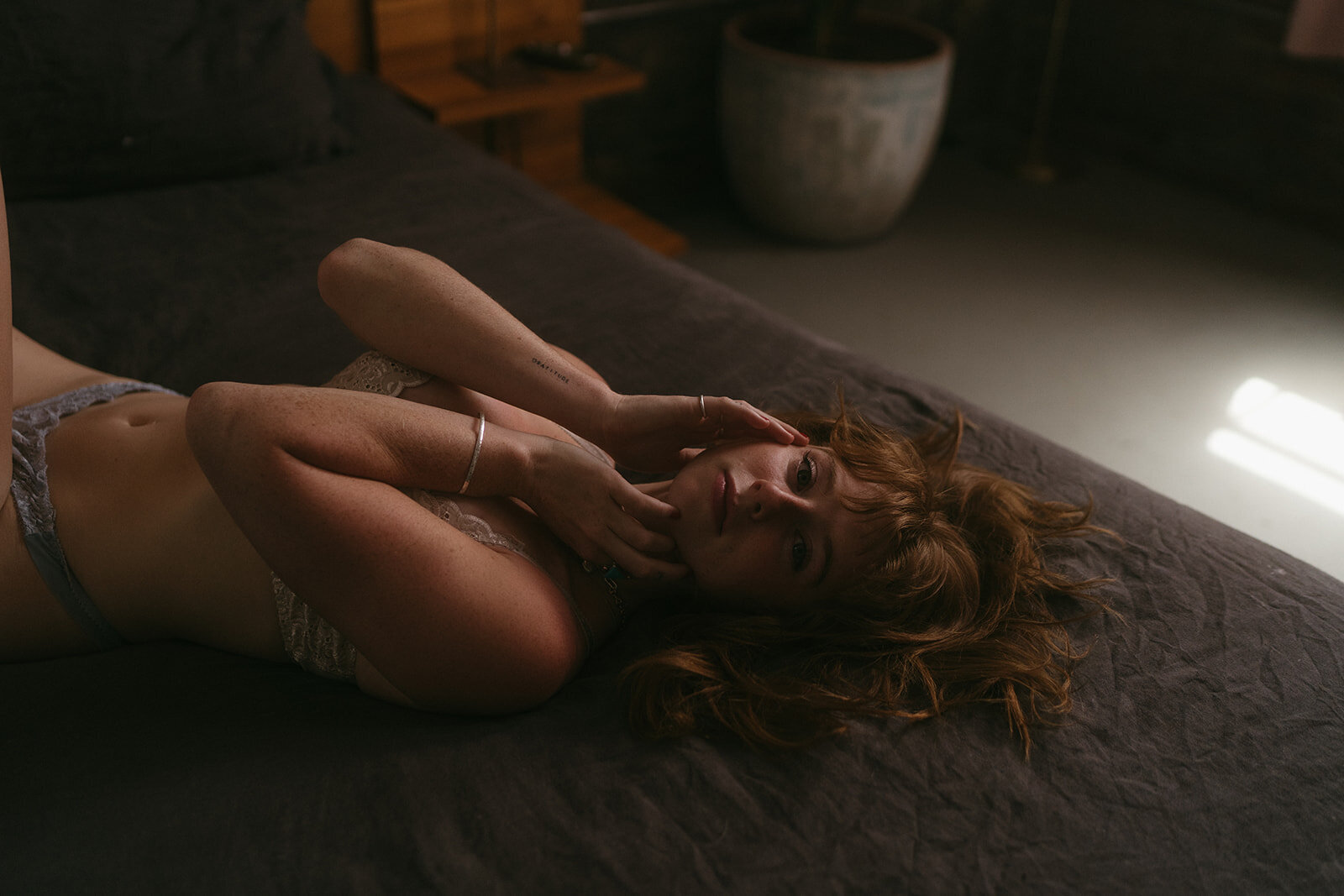Woman touches face and looks at camera while taking boudoir photos in NYC with Elsie Goodman.