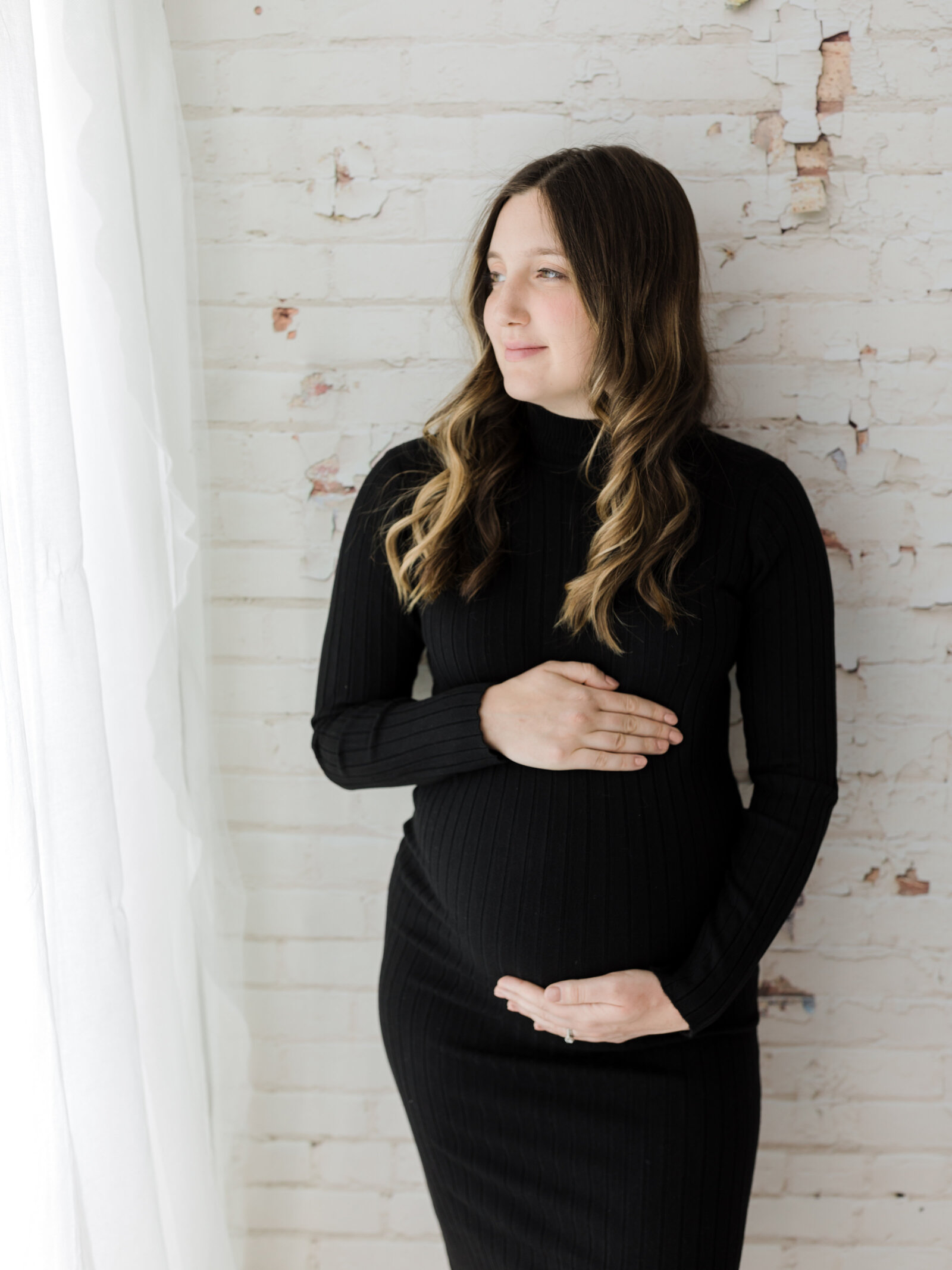 pregnant mother in black maternity dress holding baby bump for studio maternity photoshoot