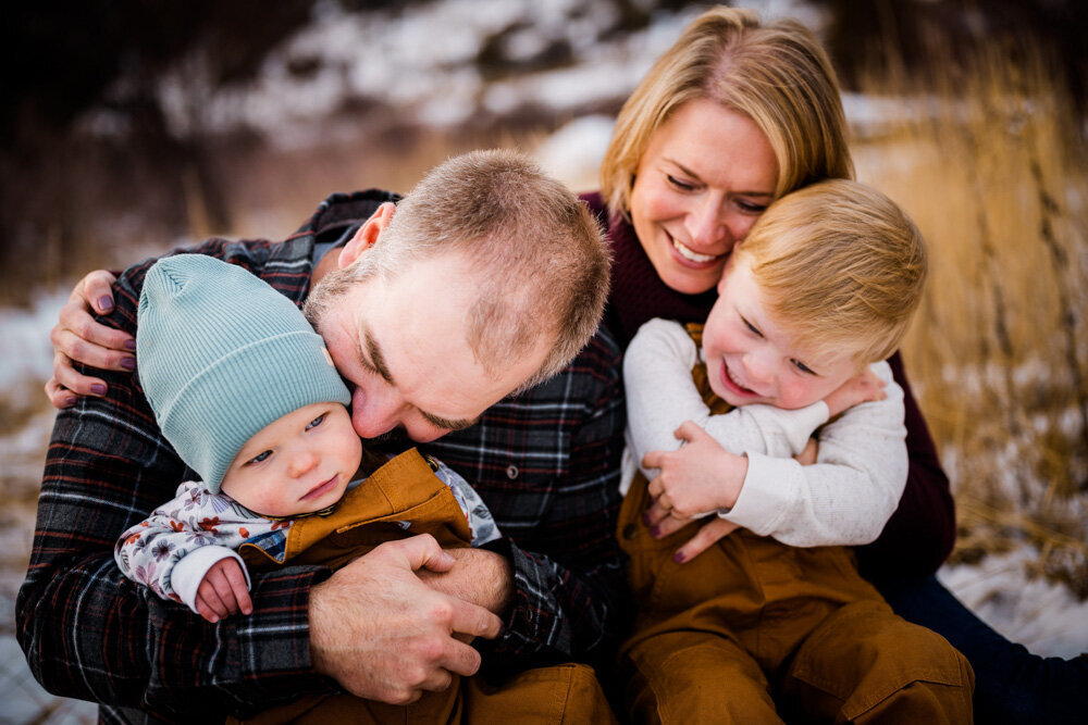 a mom and dad snuggle with their two children in a field