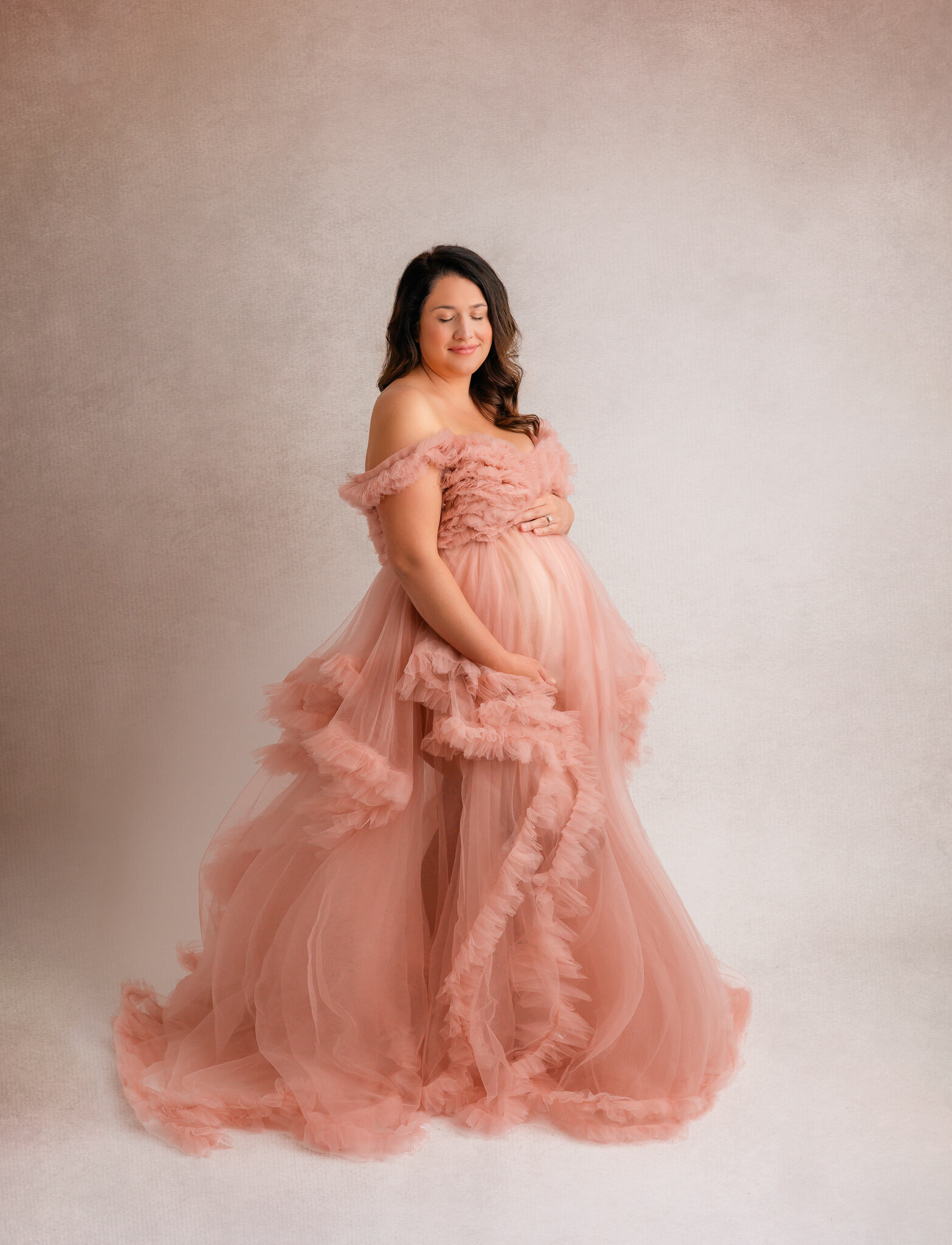Mom wearing a pink dress holding belly during maternity photoshoot in studio