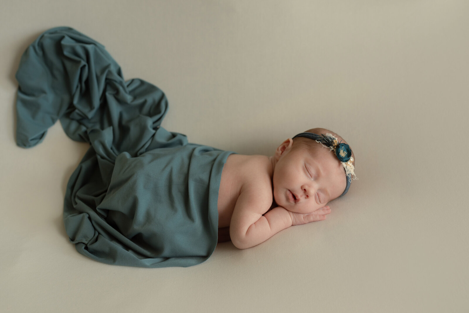 Newborn on belly posed with teal blue wrap and dried flower teal blue headband