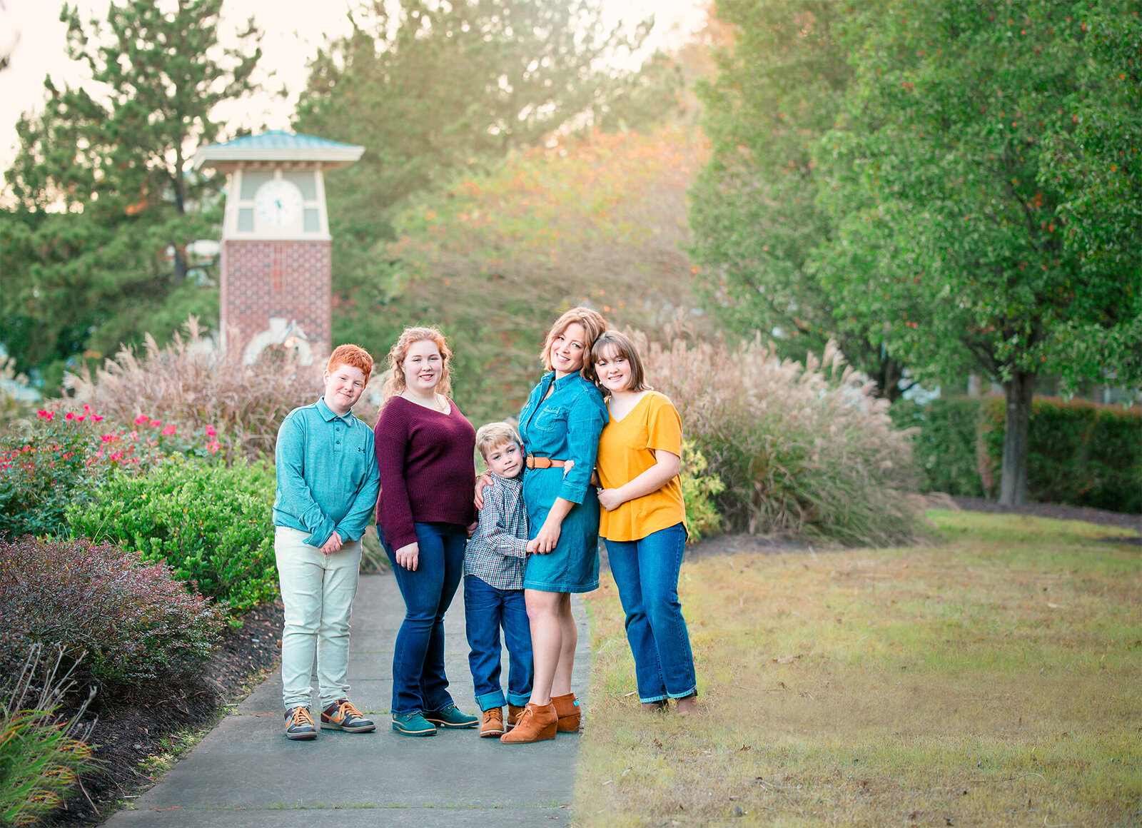 Family photographer Hampton Roads va captures outdoor spring family photos with parents and their children standing on the sidewalk in a garden with the sun beaming down above them