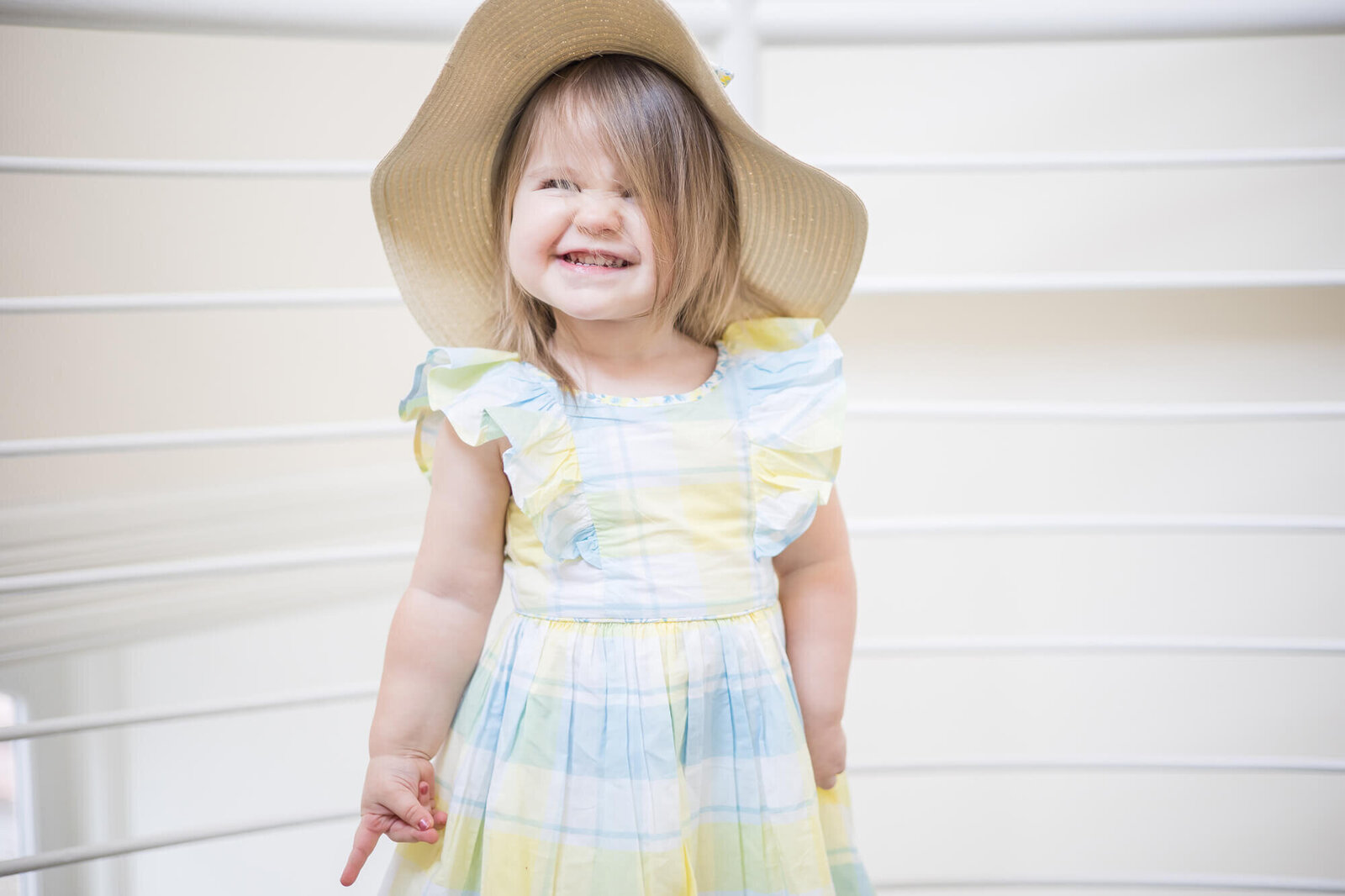 Cheesy smile on a toddler girl wearing a hat and spring sundress