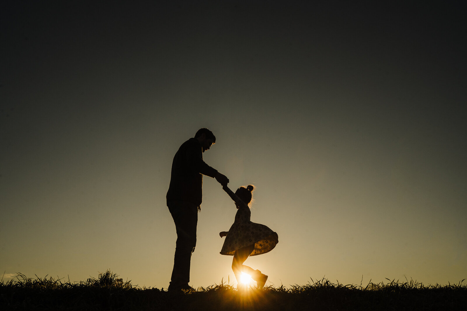 silhouette of dad spinning daughter