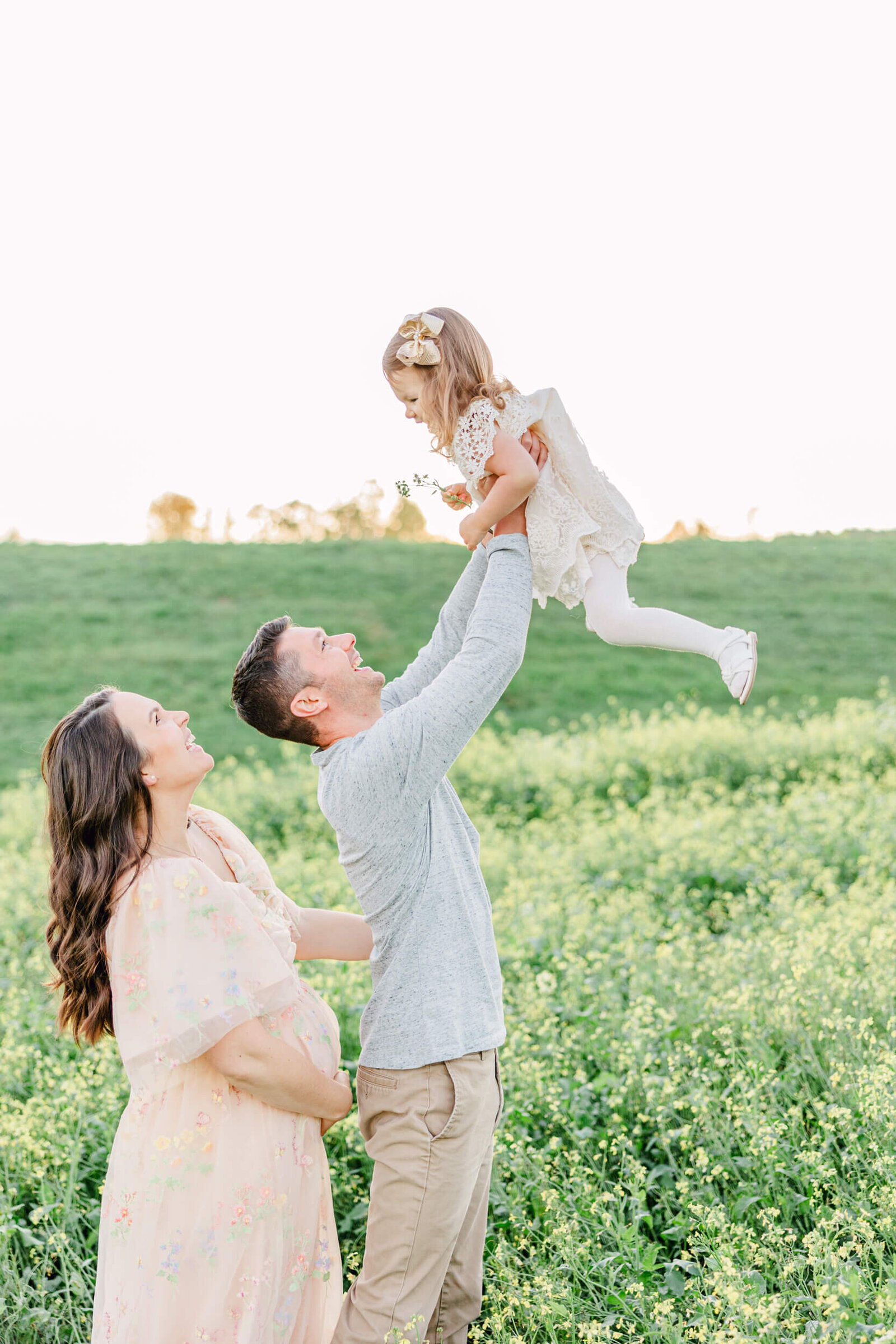 Dad tosses his young daughter in the air while pregnant mom laughs and stands behind