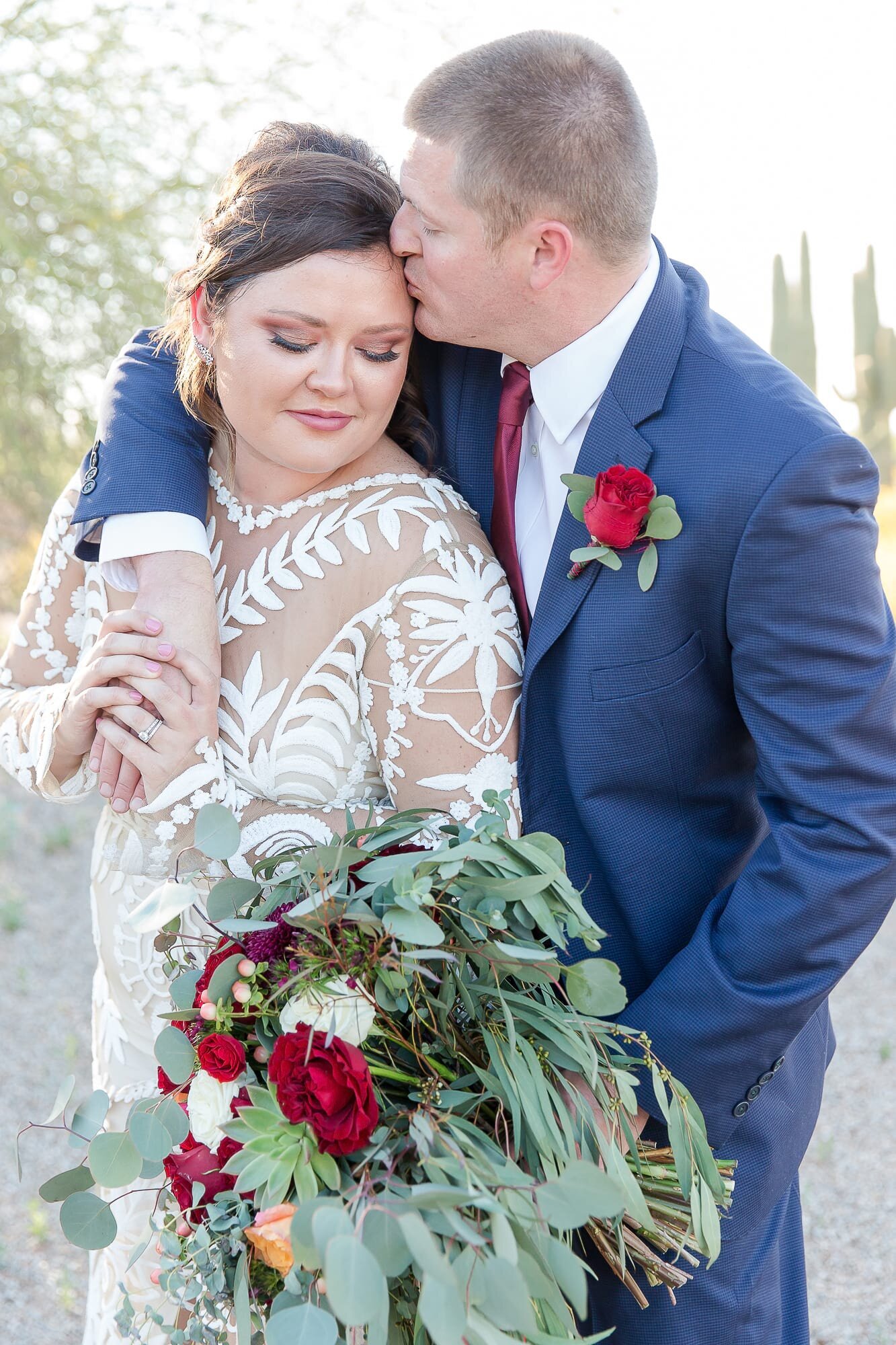 groom-kissing-bride-with-red-flowers-riparian-preserve