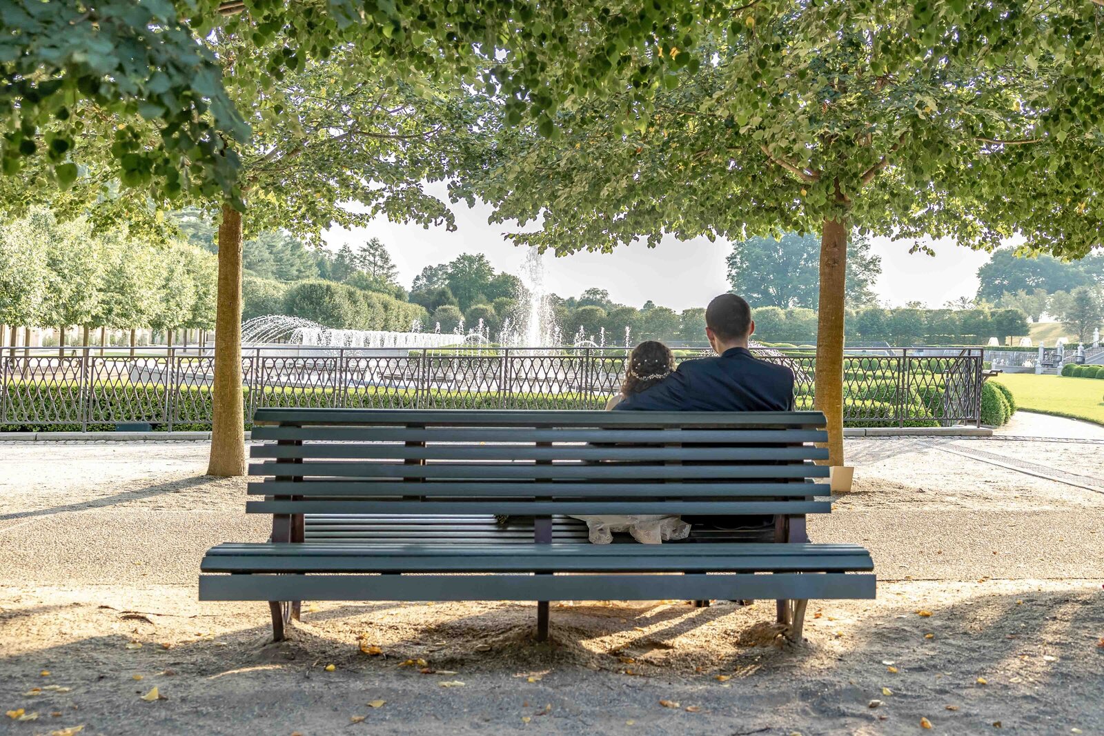 Newlyweds sitting together on a park bench at Longwood Gardens, enjoying a quiet moment watching the water fountains together, captured in Kennett Square PA.