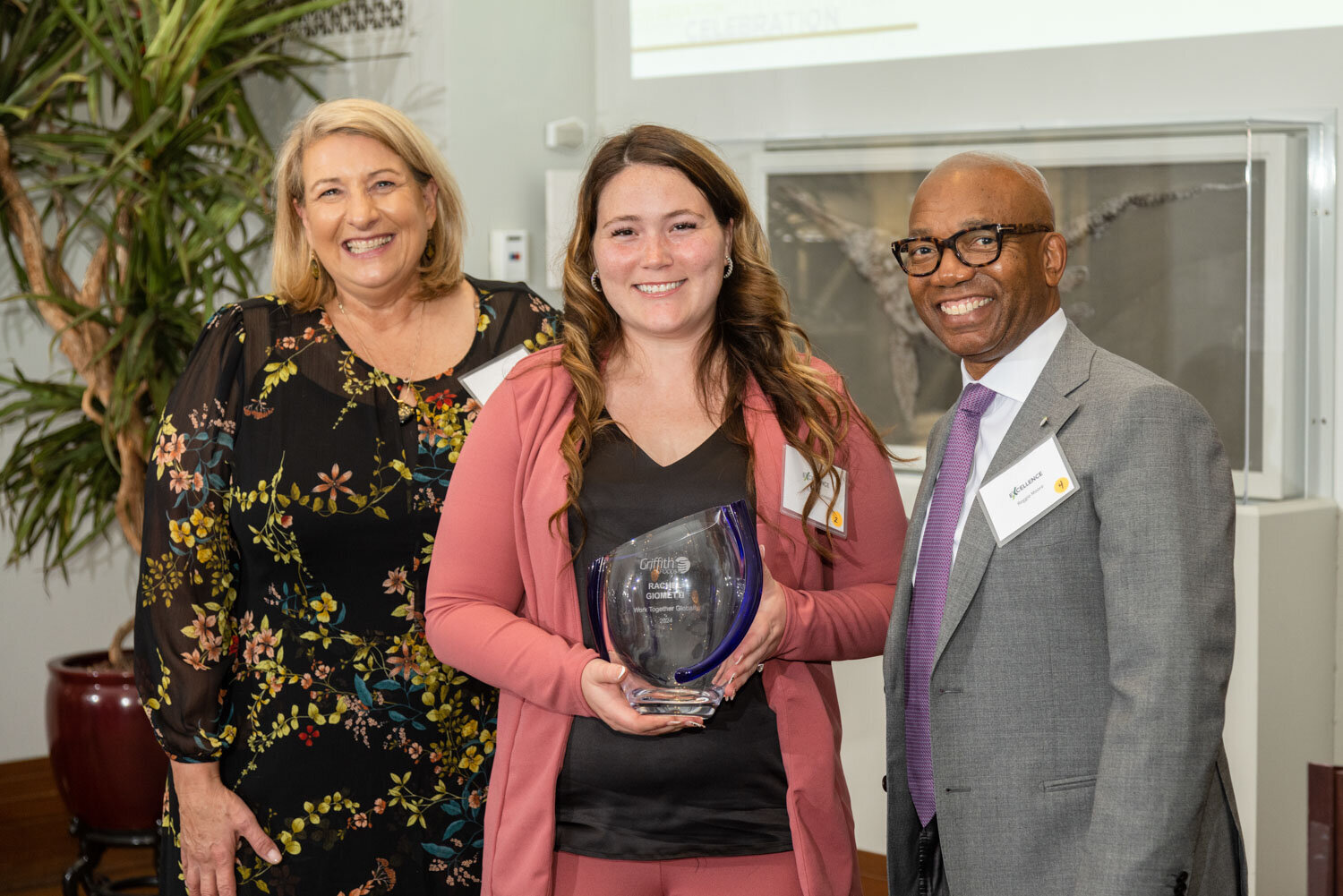 Three people smiling, one holding an award at a recognition event
