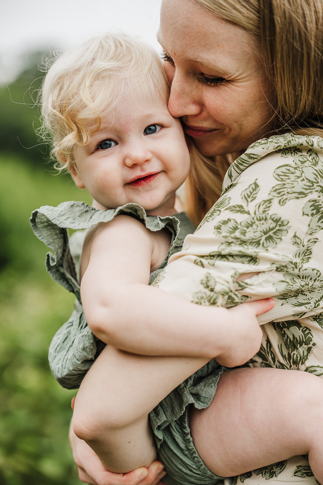 mom kisses on year old baby girl in green floral dress