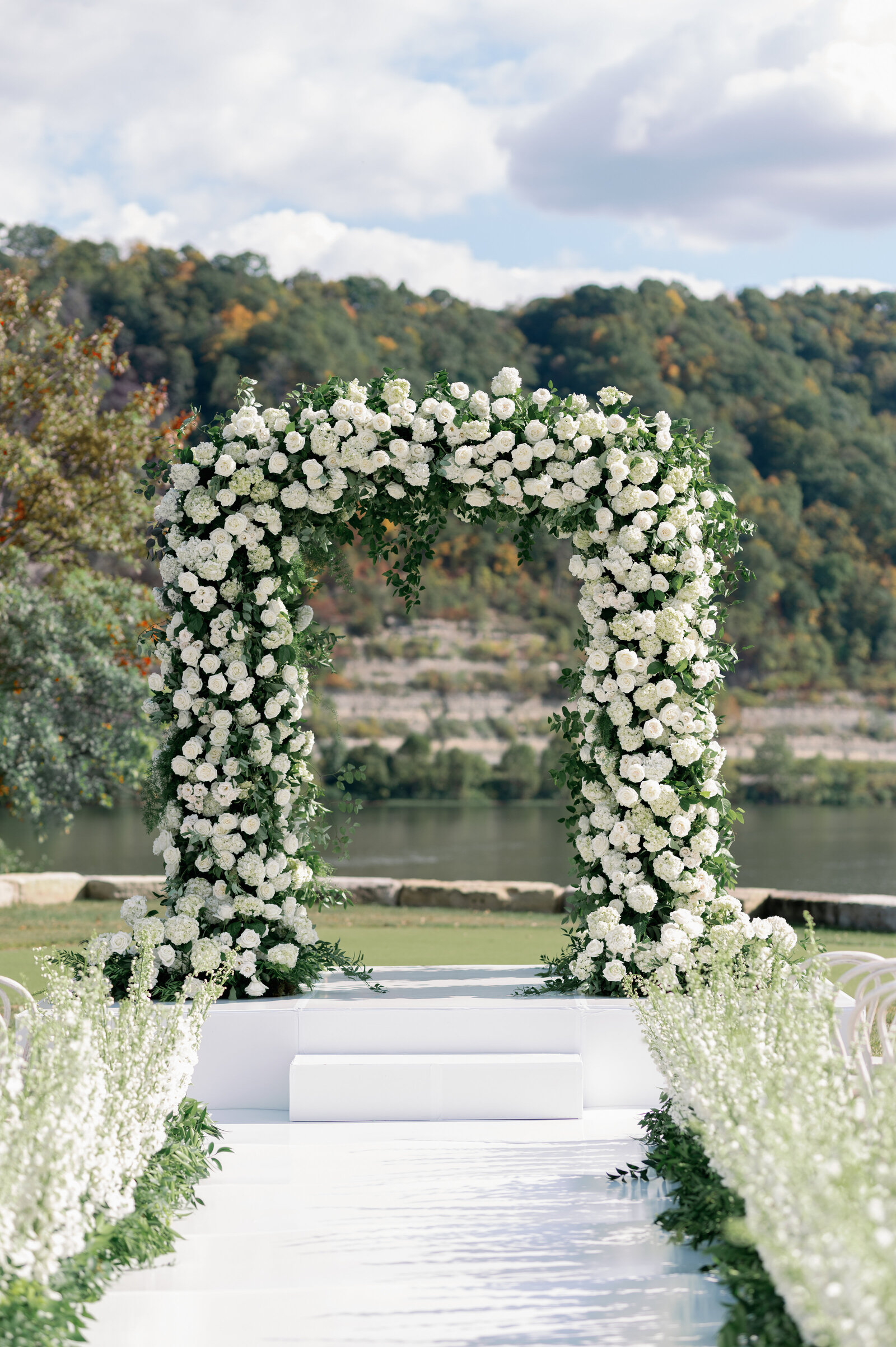 White and green floral arch at outdoor wedding near lake