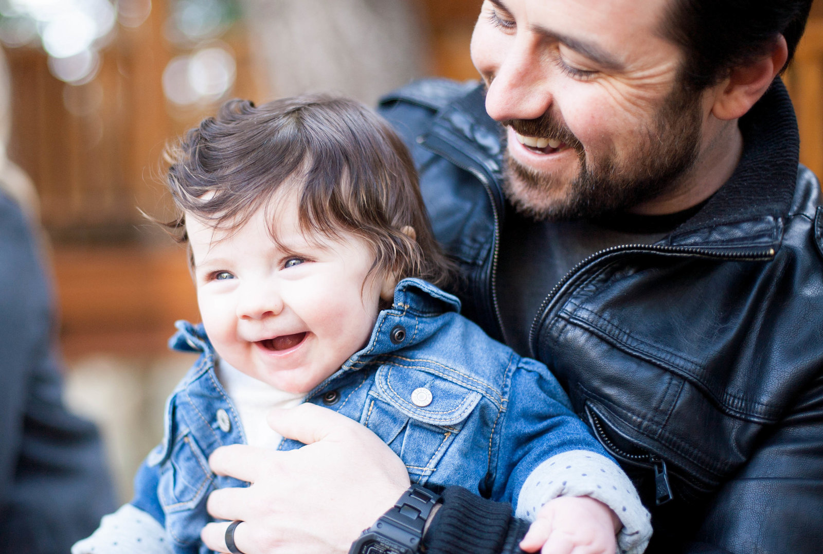 A father in a leather jacket holding his son, in a denim jacket.