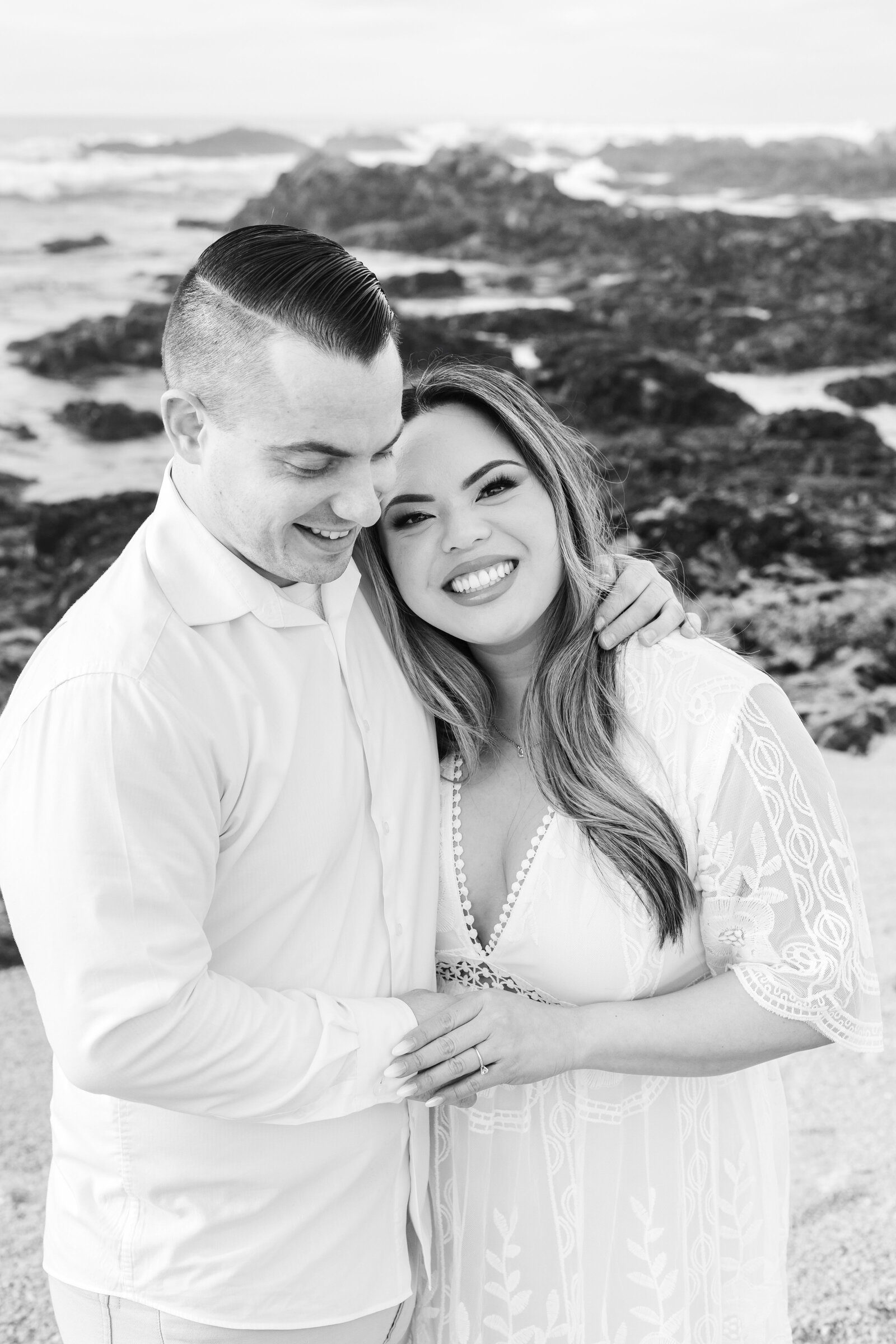 An engaged man and woman take photos on the beach in Pacific Grove, Monterey, California near Big Sur.